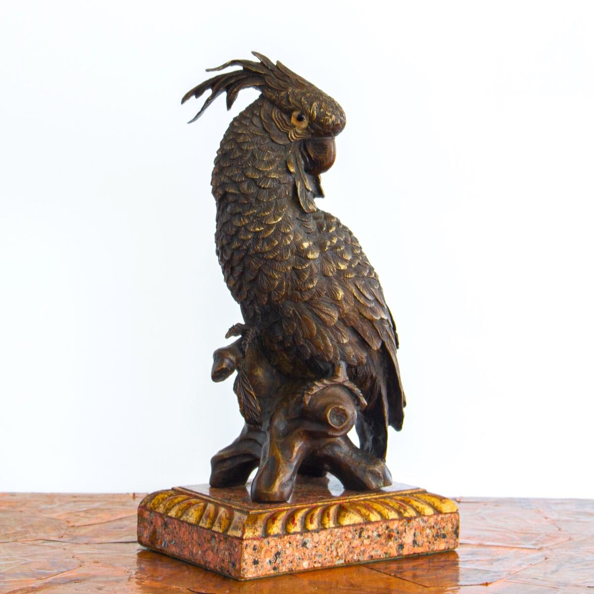 A 20th century, intricately carved bronze crested parrot with glass eyes, perched on a branch and mounted on a mottled marble and gilt acanthus base.