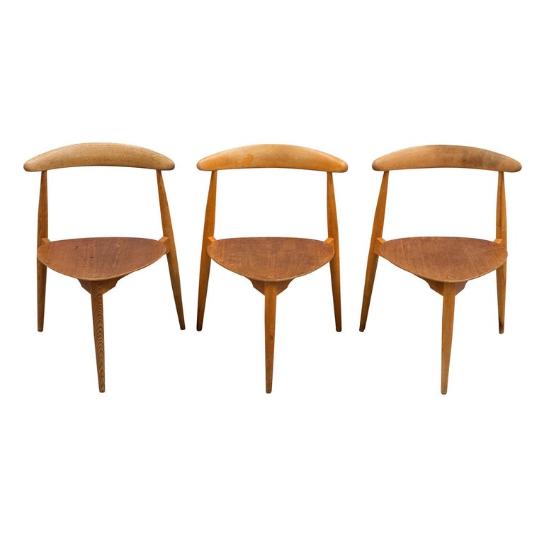 A vintage Mid-Century Modern Danish set of three side chairs made of hand carved teak wood, designed by Hans J. Wegner and produced by Fritz Hansen with heart shaped seats, three sculpted legs and seat backs, in good condition. Model H 4013. Wear