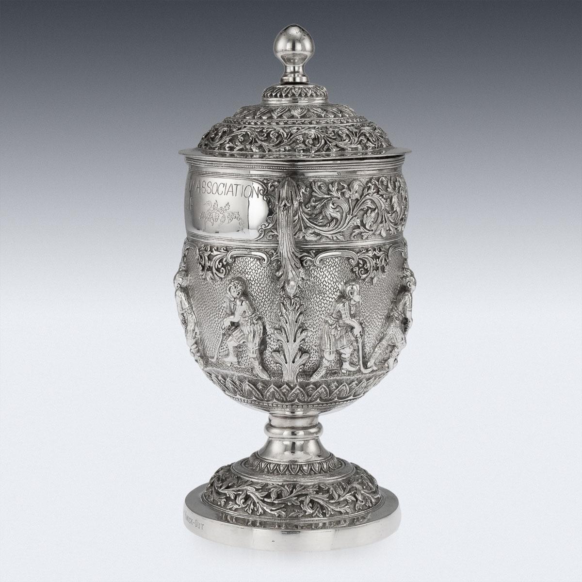 Antique early 20th Century Burmese (Myanmar) solid silver hockey trophy, of traditional shape, highly-decorative, the body embossed with hockey players Burmese vs Europeans, below a chased border of foliate scroll decoration, applied with leaf