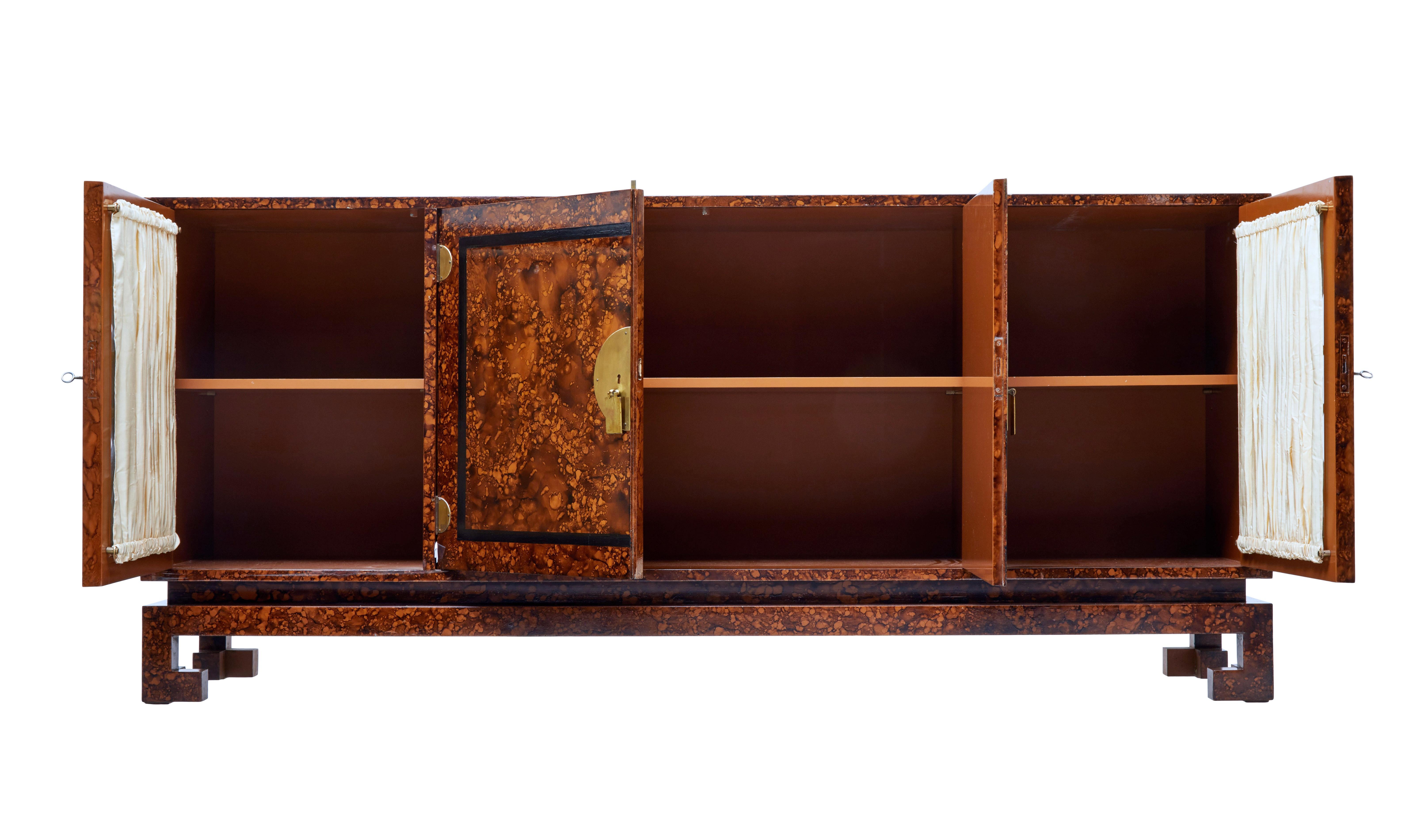 Exotic burr veneered sideboard in the Art Deco style, with strong Chinese influences.

Four-door sideboard with a central double door cupboard containing a single shelf, flanked either by a single door cupboard containing a shelf. Black fret work