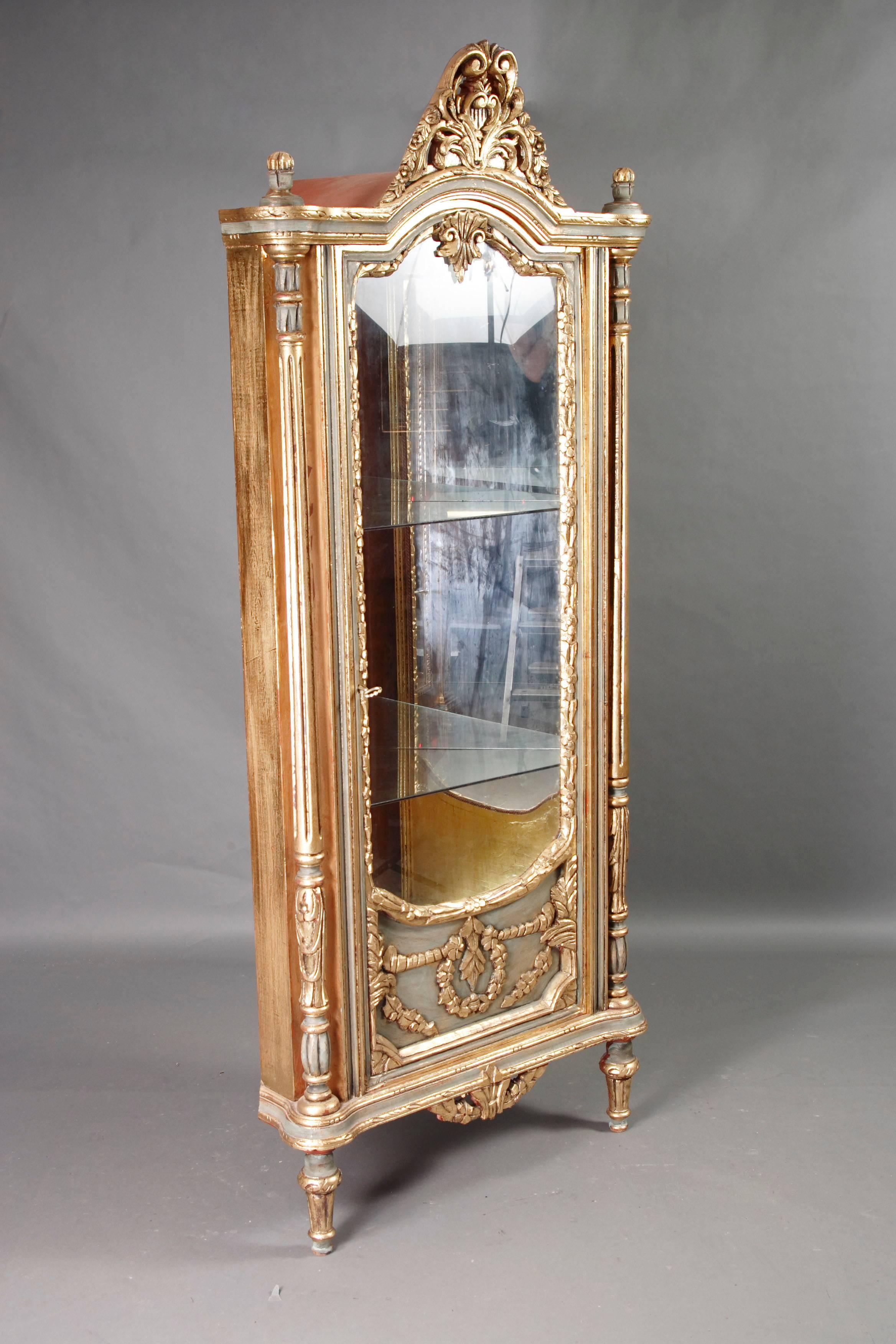 Solid beechwood, carved, colored and polished gold-plated. High-right corpus on conical furled legs. Three-quarter glazed door, flanked by carved full columns.
Ornately carved crown. Two glassy floors, rear wall mirrored.
 