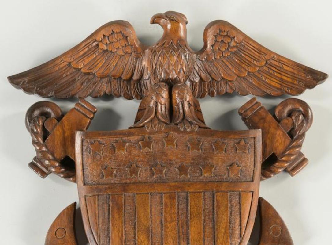 This is a stunning 20th century carving of an eagle with shield. The carved piece depicts the U.S. Navy emblem. There is a large eagle on the top, with widely spread wings and an arched beak. The eagle rests on an American shield, with stars and