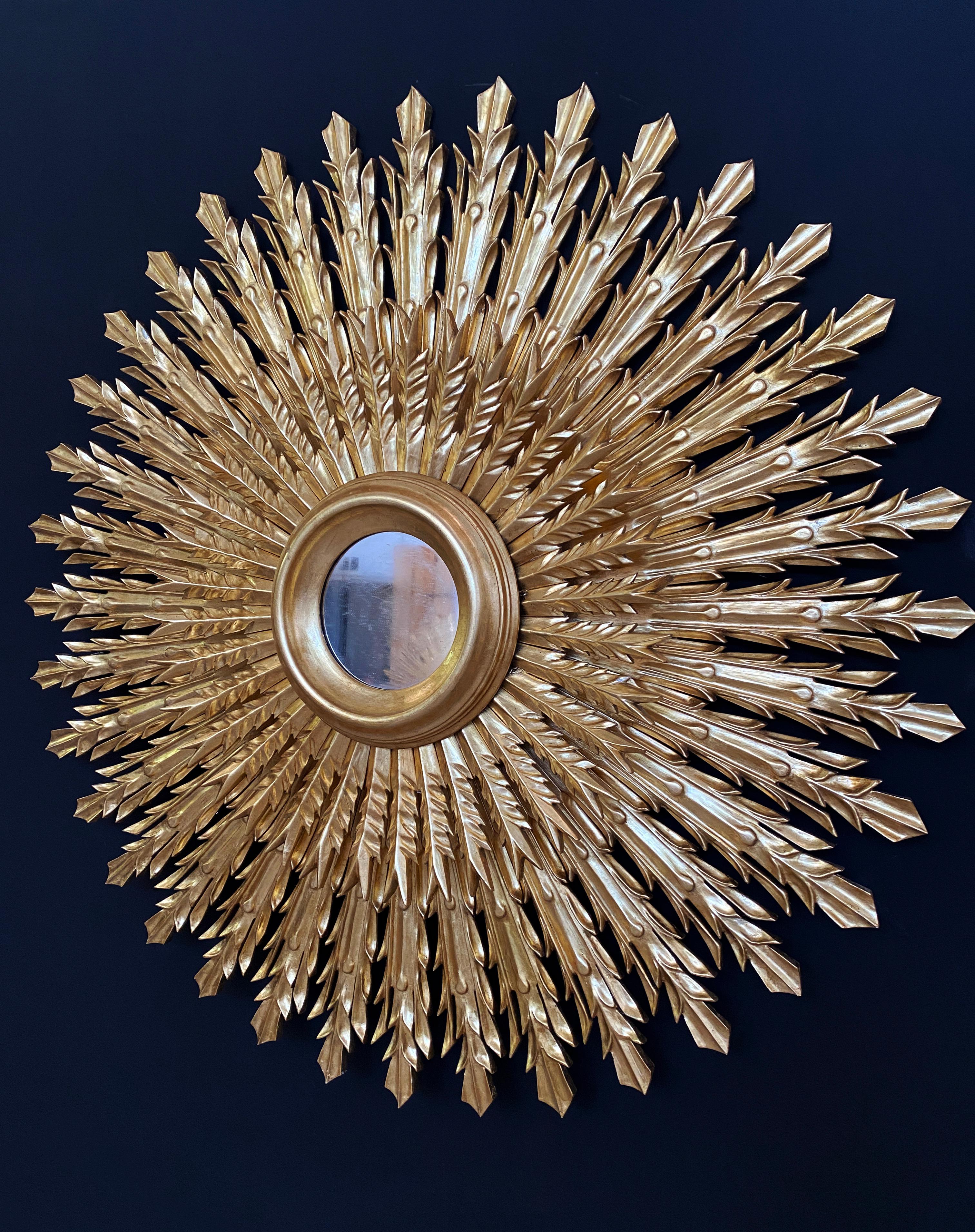 Magnífico espejo dorado con efecto sol. Esta exquisita pieza se talló totalmente a mano y presenta dos niveles de rayos de madera dorada, cada uno de ellos con una forma única para crear un diseño llamativo y armonioso. Cada rayo se esculpía