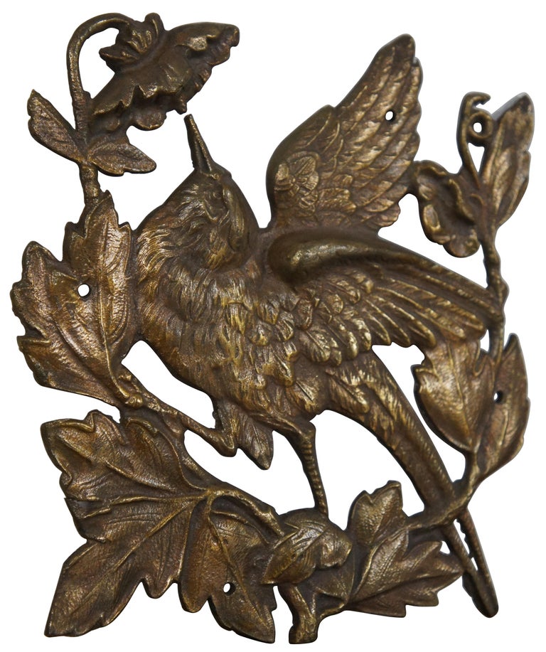 Vintage cast bronze wall plaque in the shape of a bird perched on a leafy branch with two flowers.


