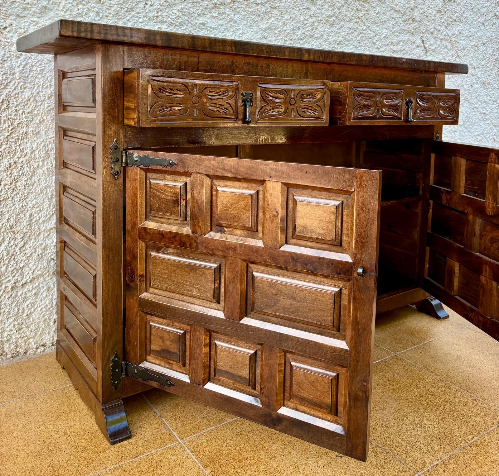 Katalanische, spanische, geschnitzte Nussbaumkommode, Anrichte oder Konsole aus massivem Nussbaum mit zwei geschnitzten Schubladen, zwei charmant detaillierten Türen mit gusseisernen Griffen und einem großen Regal, ca. 1920er Jahre.