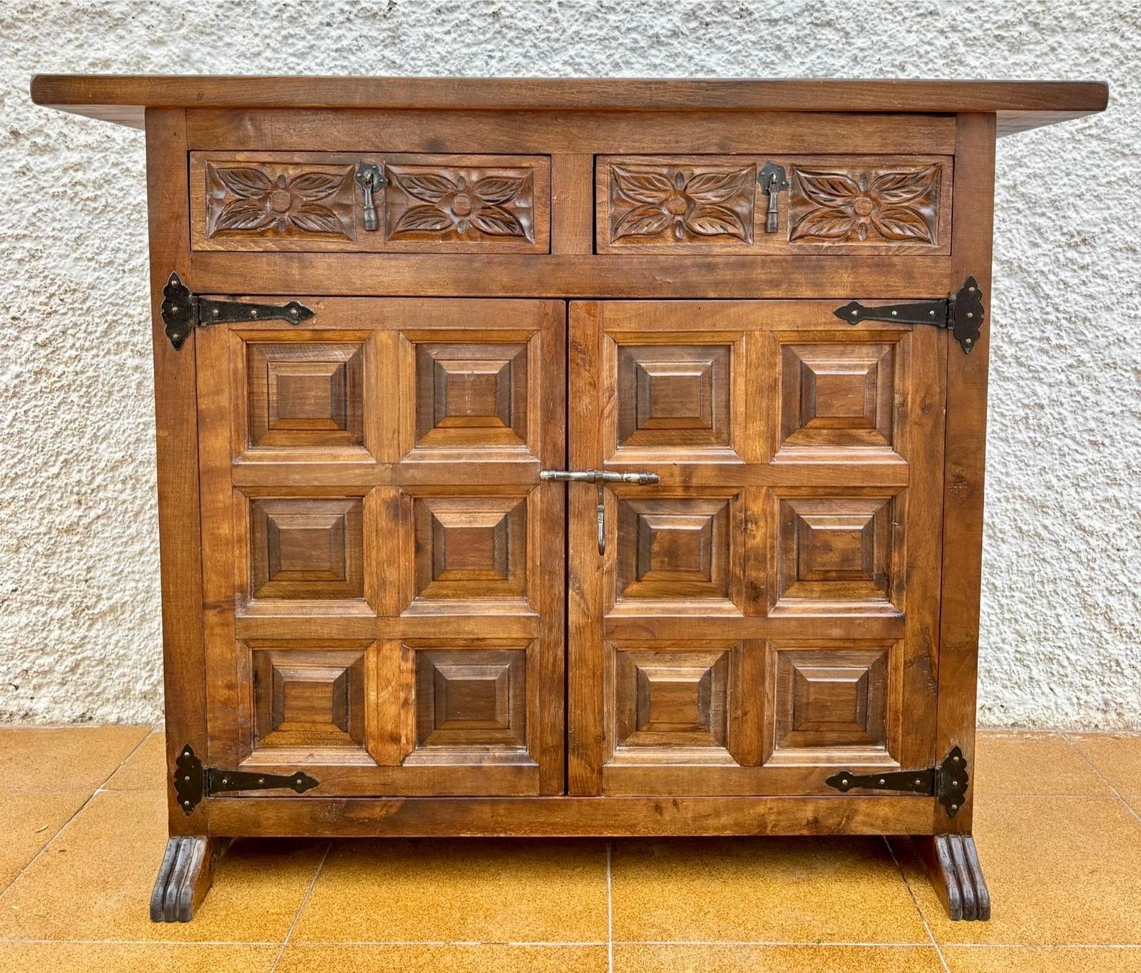 Old Castilian chest of drawers from the early 20th century with two front doors decorated with panels and iron fittings and two drawers carved with floral motifs with iron dilators.
The sides are also decorated with panels.