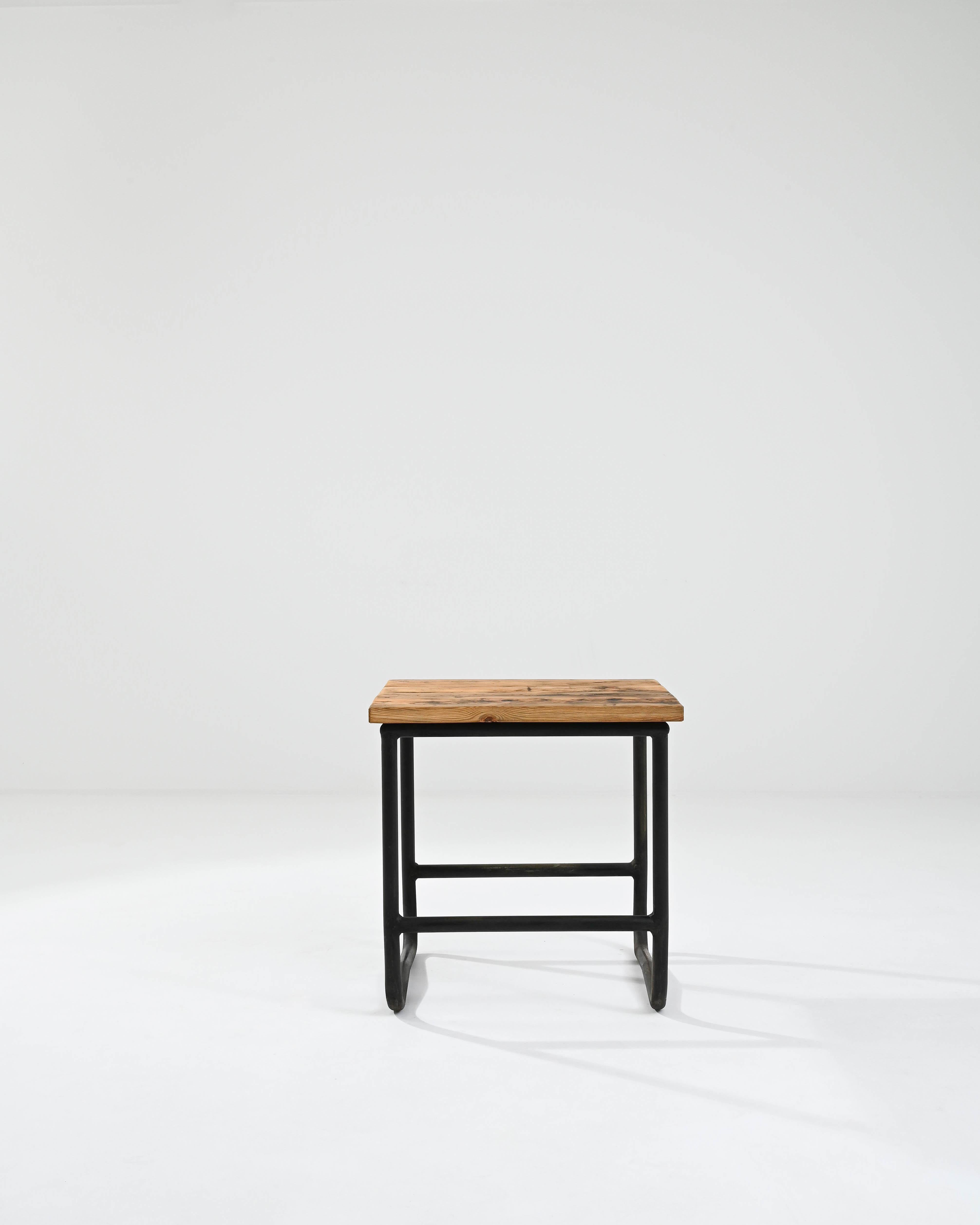 A metal side table with a wooden top made in 20th century central Europe. This stout and amicable side table greets one with a demeanor of an bold yet charmingly reliable companion. Black steel tubes have been welded together, with a subtle kink