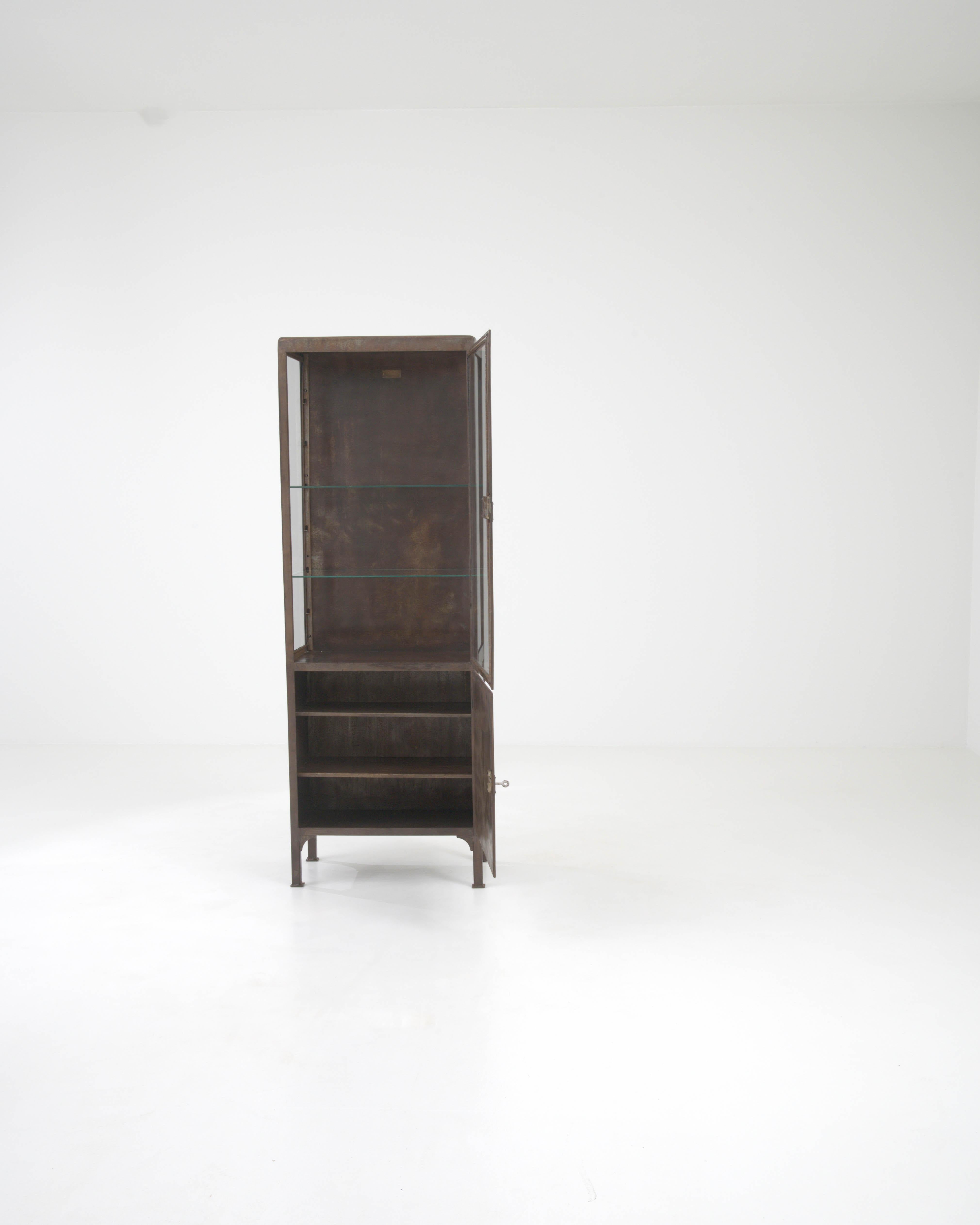 Step into the past with this authentic 20th Century Central European Metal Vitrine, a treasure trove for collectors and interior design aficionados alike. Crafted with precision, this slim, upright cabinet pairs the industrial charm of its dark