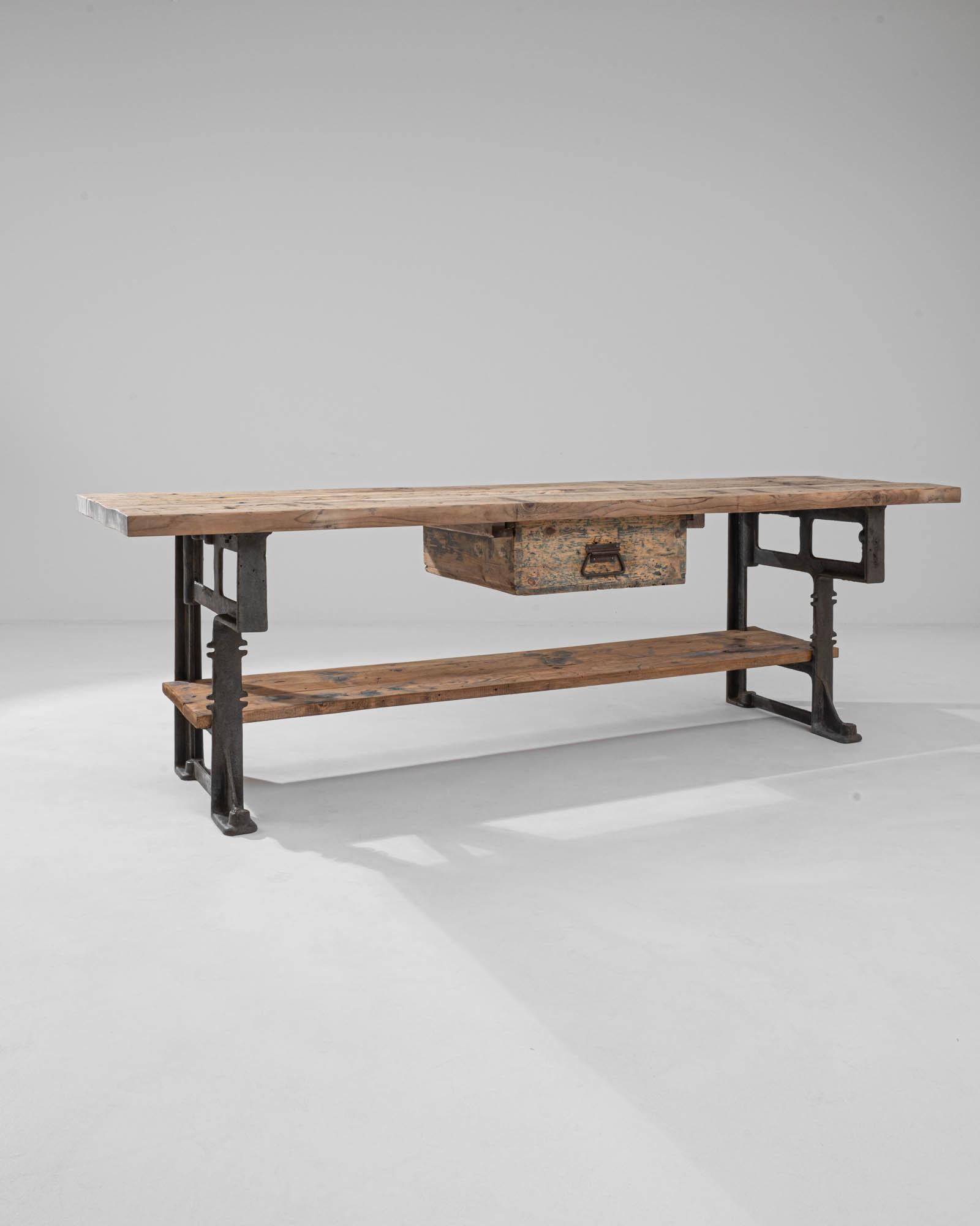 The bold Industrial aesthetic of this vintage work table combines practicality with vigor. Made in Central Europe in the 20th century, the planks of the wooden tabletop provide a generous and sturdy work surface, while the solid, angular silhouette