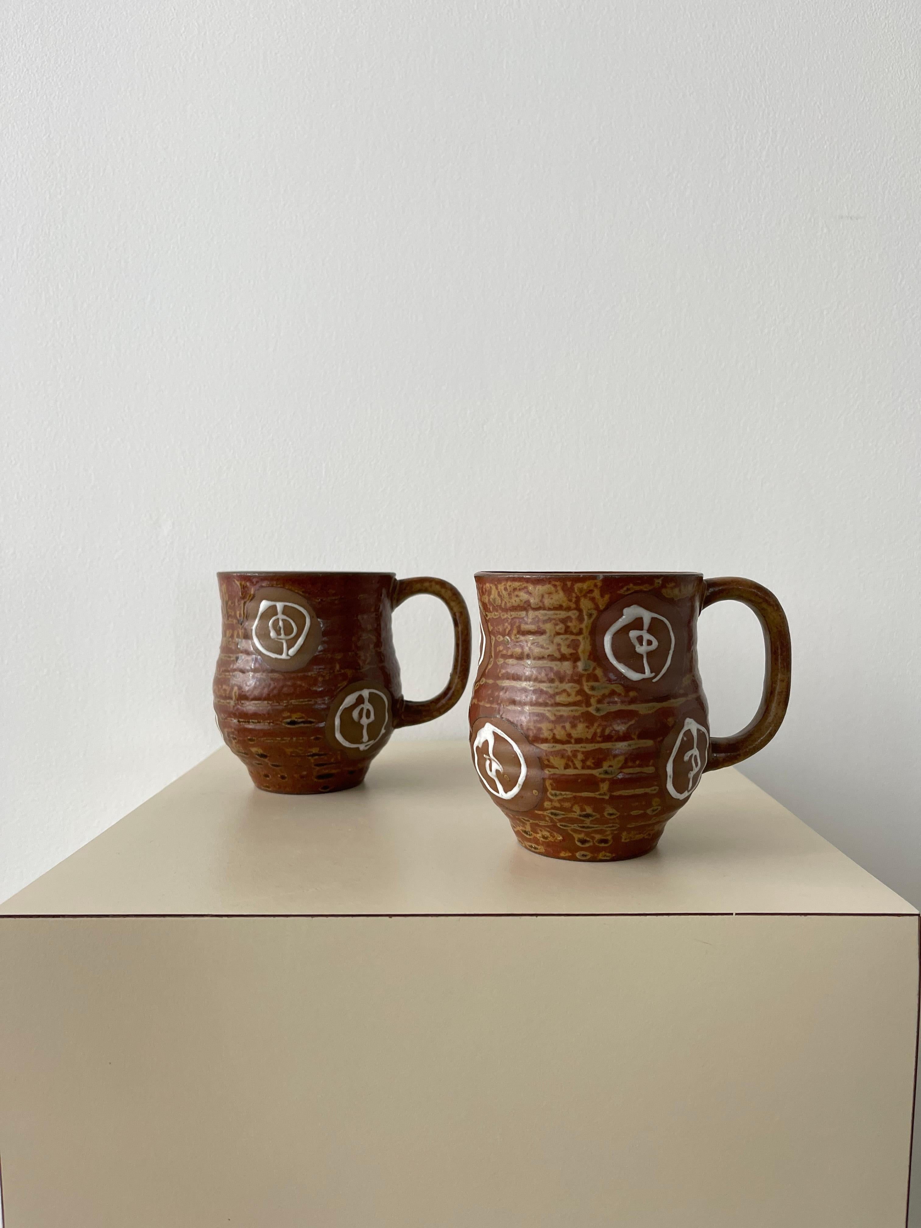 20th Century Ceramic mugs in a multi colored brown colorway with a unique glazed finish and design that resembles freeform bullseyes. Unique ridged texture with handles and a fluted opening.