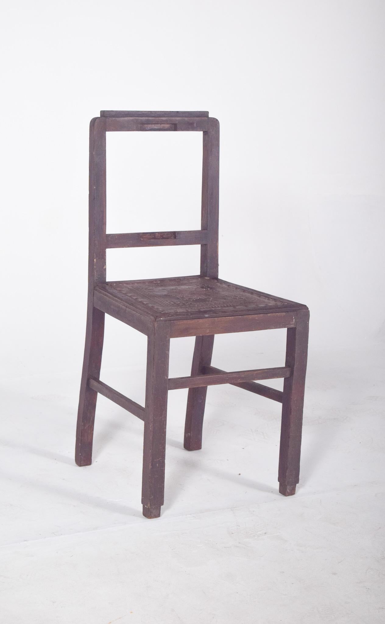 Stuhl mit geprägtem Ledersitz und Nagelkopfverzierung. Schlichte, robuste Linien, ein Gestell aus dunklem Holz und eine Sitzfläche aus geprägtem Leder, reich verziert mit floralen und geometrischen Mustern im Flachrelief. Der Rand des Sitzes ist mit