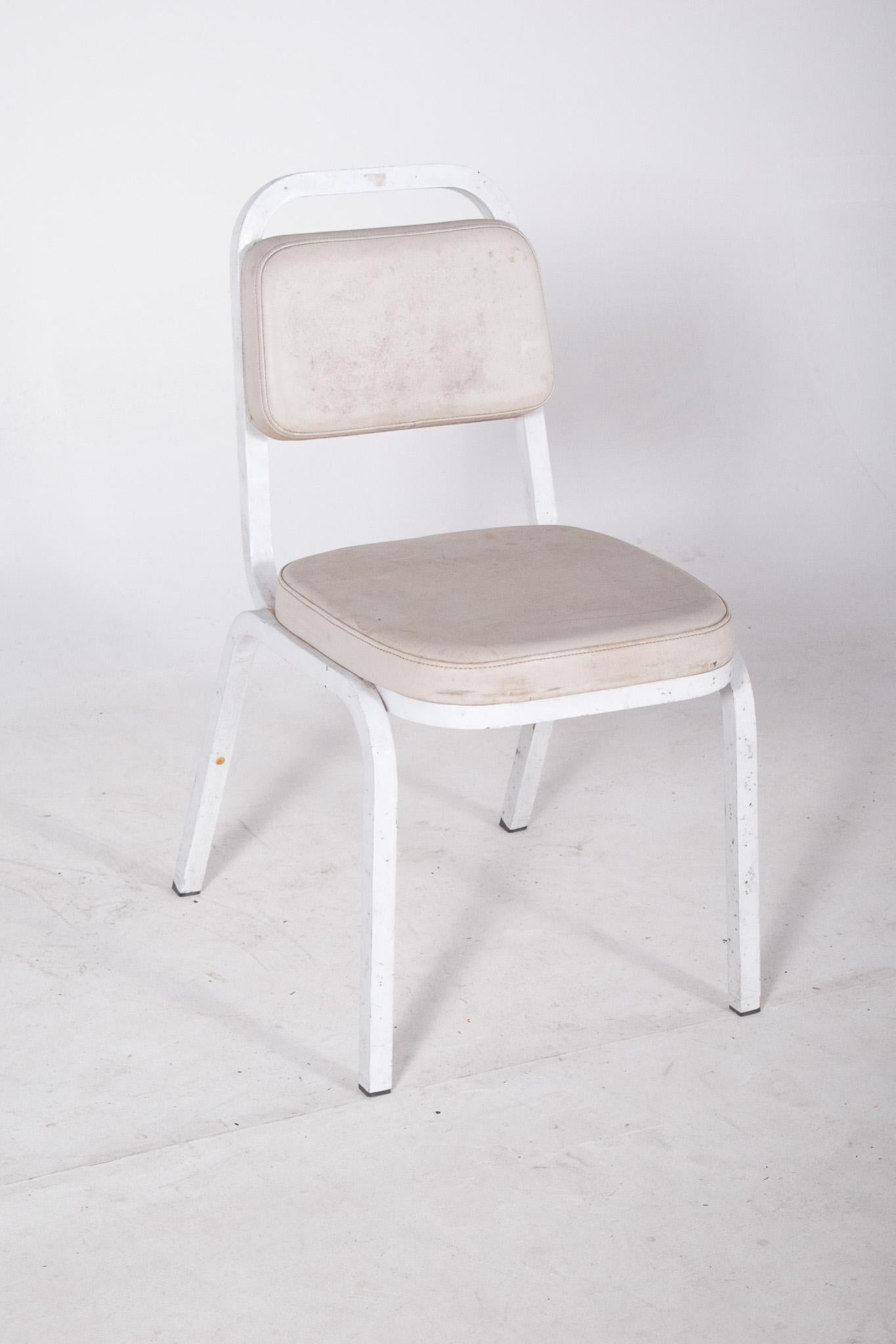 Silla con estructura y tapicería blancas. Con armazón de metal blanco y asiento y respaldo tapizados en piel sintética blanca, presenta marcas visibles de uso y desgaste, sobre todo en la parte delantera del asiento y los bordes del respaldo. El