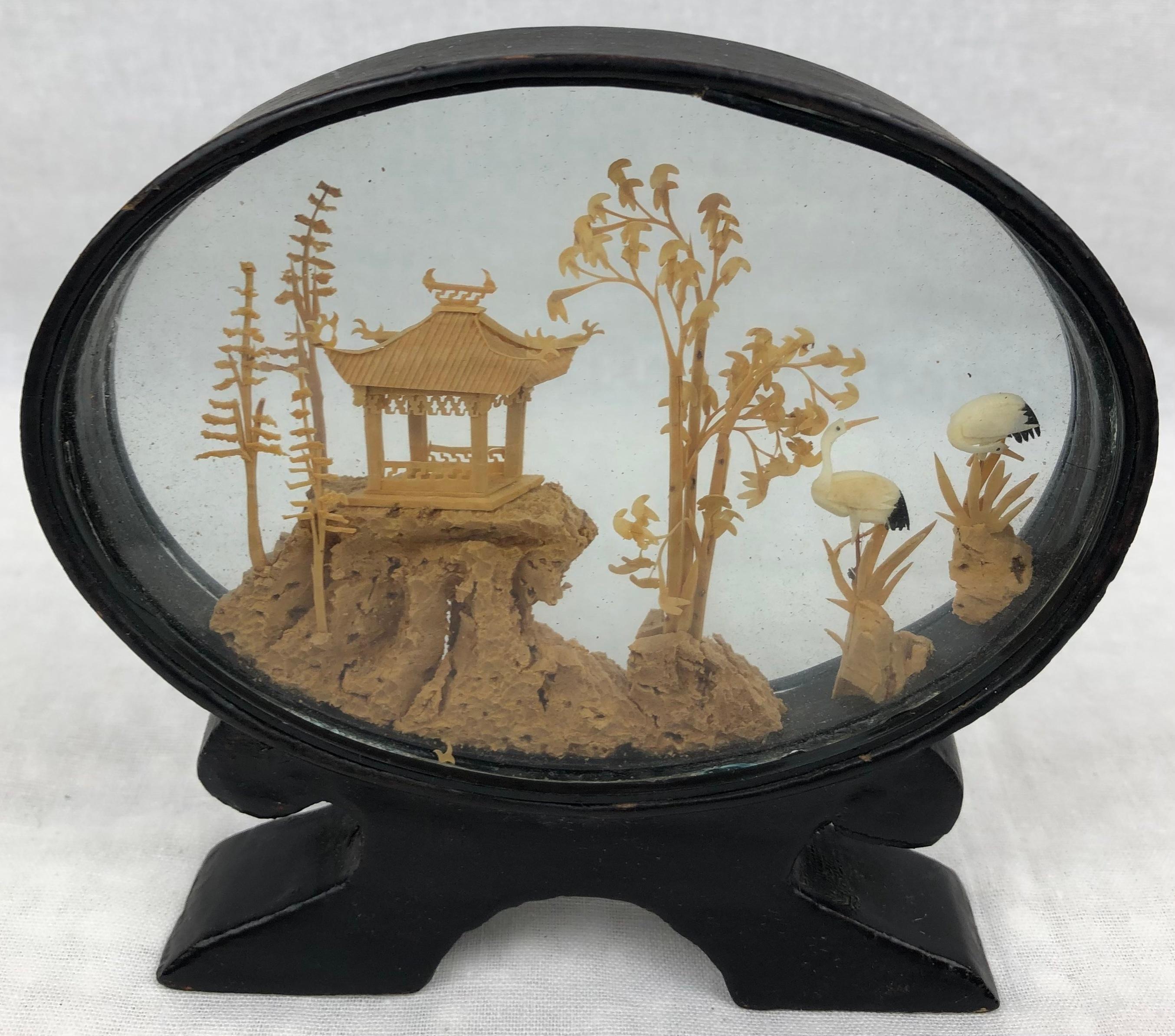 Beautiful 20th century oval Chinese cork diorama.
Finely carved decoration in a glass case and black lacquered base.
Chinese landscape view, a pagoda in a traditional garden featuring storks. 

Traditional Asian cork sculpture.