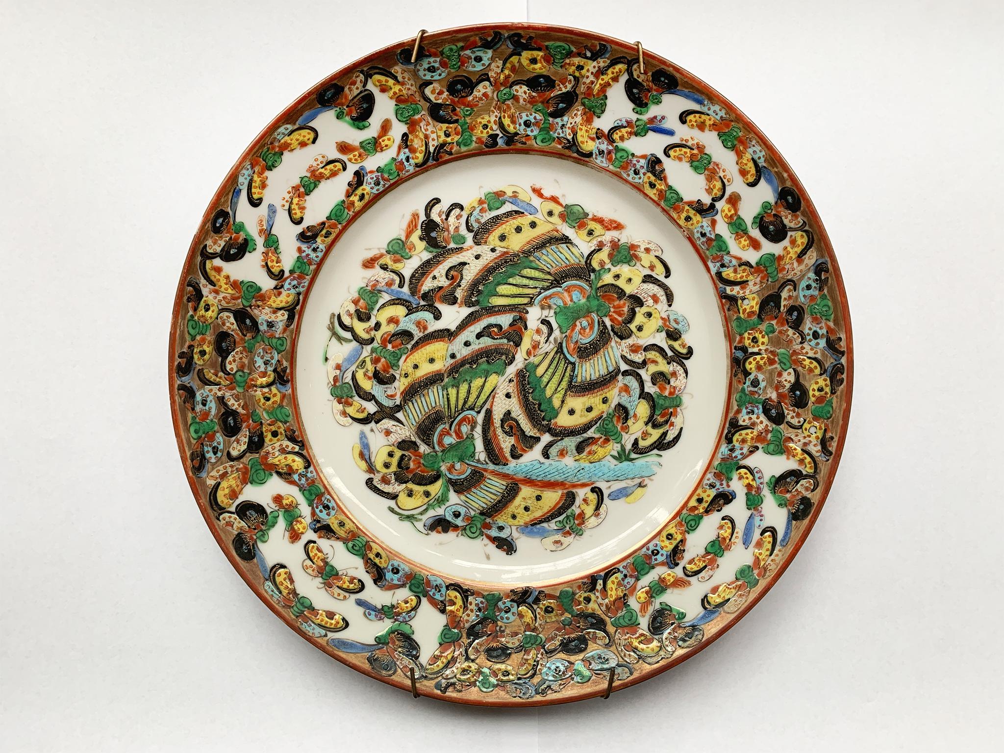 A set of six 20th century decorative porcelain plates from China. The rich, colorful design is rendered in enamel paint with a palette of reds, blues, greens, yellows, black, and gold. At center is a cluster of butterflies. The surrounding border is