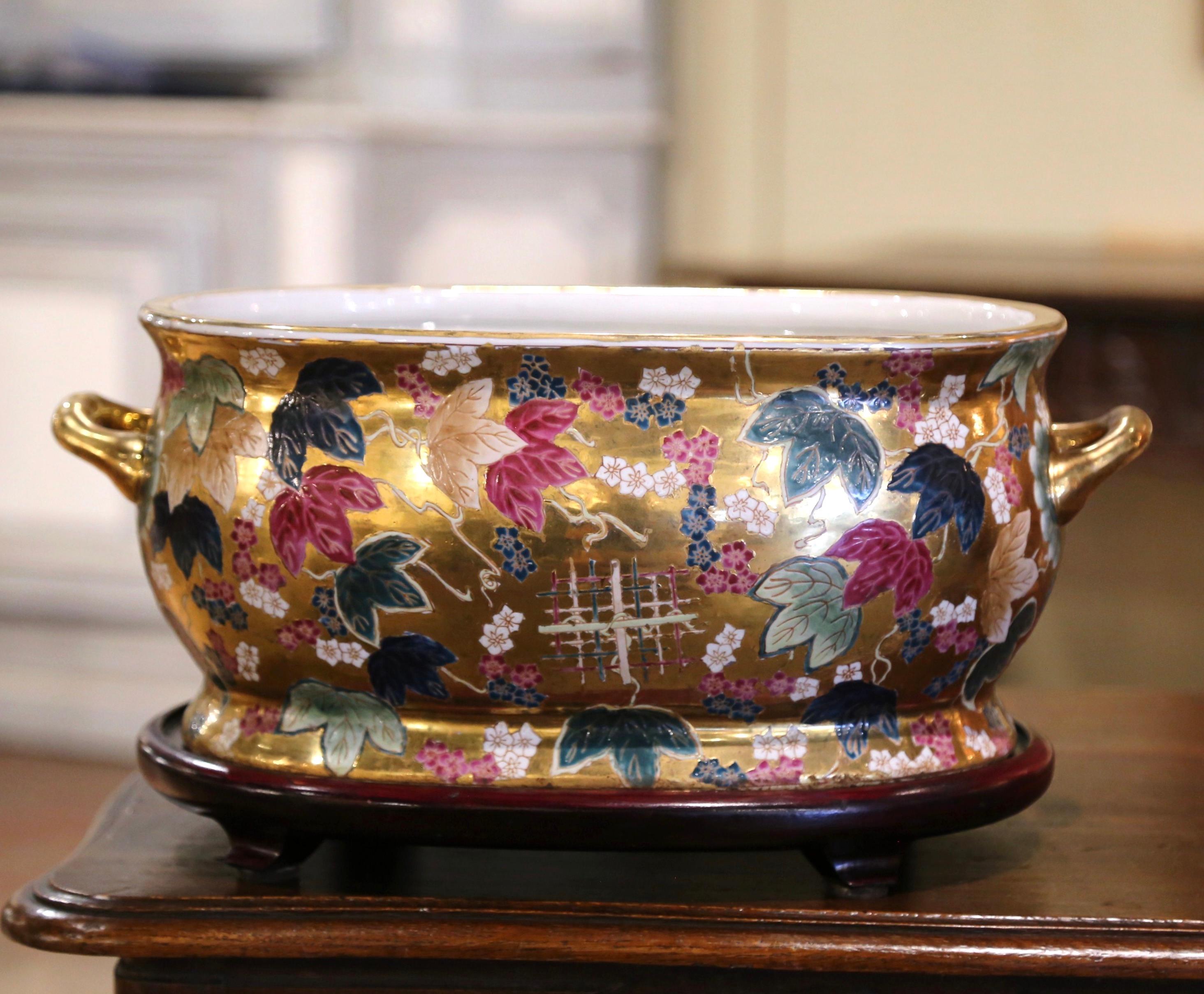 Crafted in China circa 1970, this elegant oval porcelain basin with wood base features vibrant hand-painted floral motifs in rich reds, greens, blues, and golds across its exterior. Stylized leaves and delicate blossoms adorn the surface, enhanced