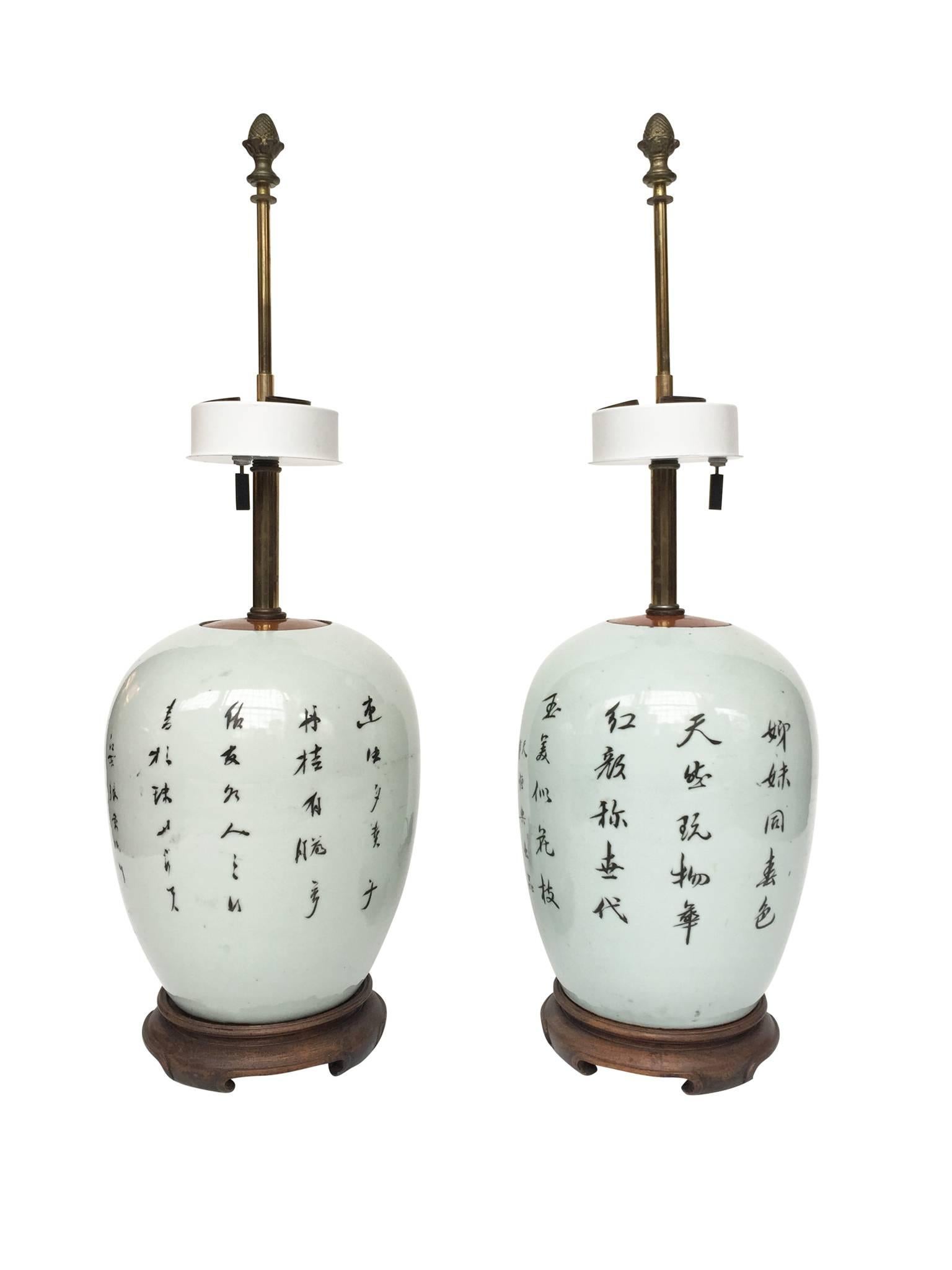 These two porcelain jar lamps have hand-painted figures in idyllic landscapes on one side, and hand-written calligraphy in black on the other. The jars are covered with wood in a glossy finish, while their bases are a reddish brown wood. The lamps