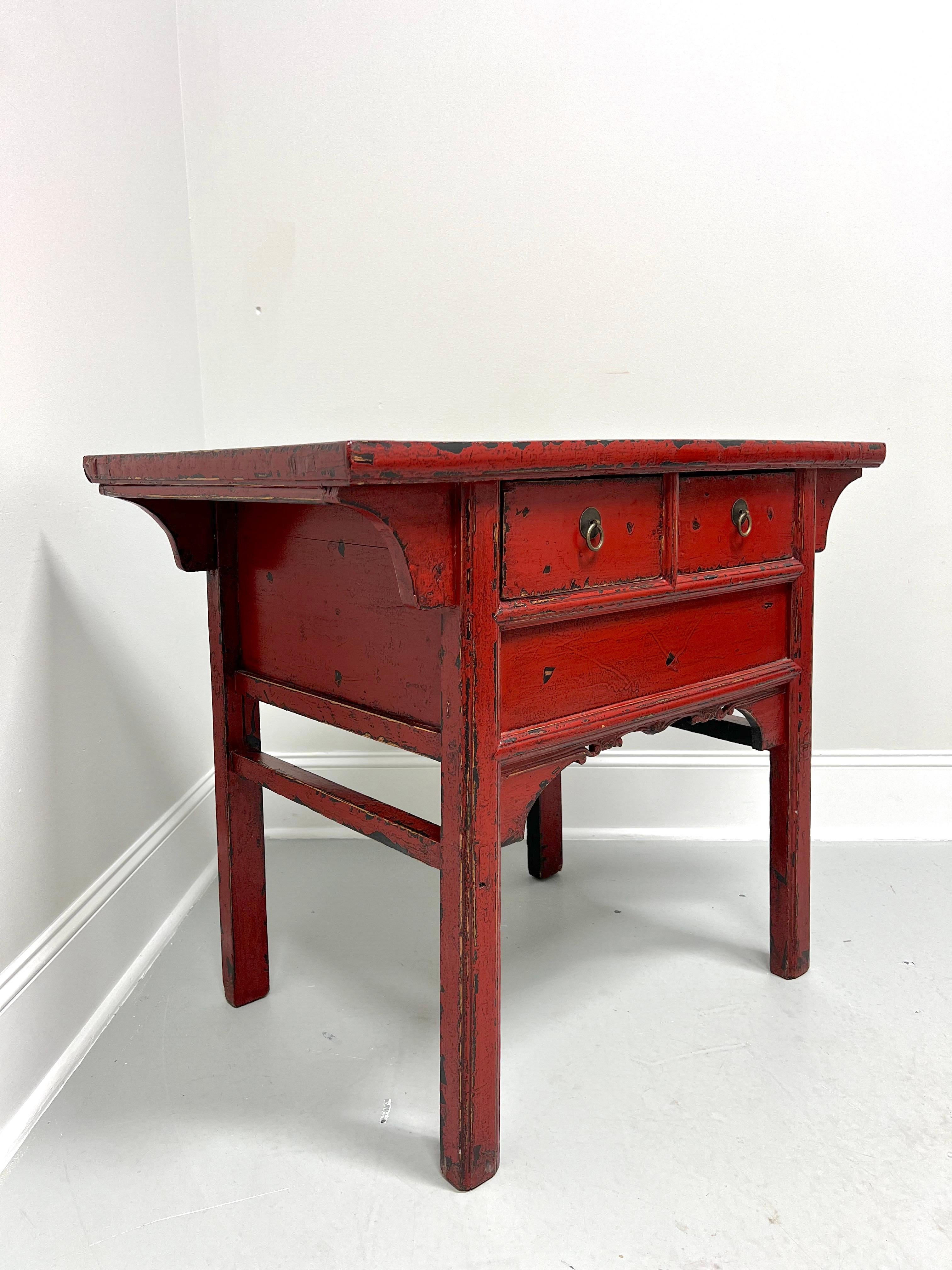An Asian Chinese altar table, unbranded. Solid wood painted red, distressed to give appearance of advanced age, brass hardware, banded plank top with smooth edge, carved angular sides, carved apron, and square straight legs. Features two drawers of