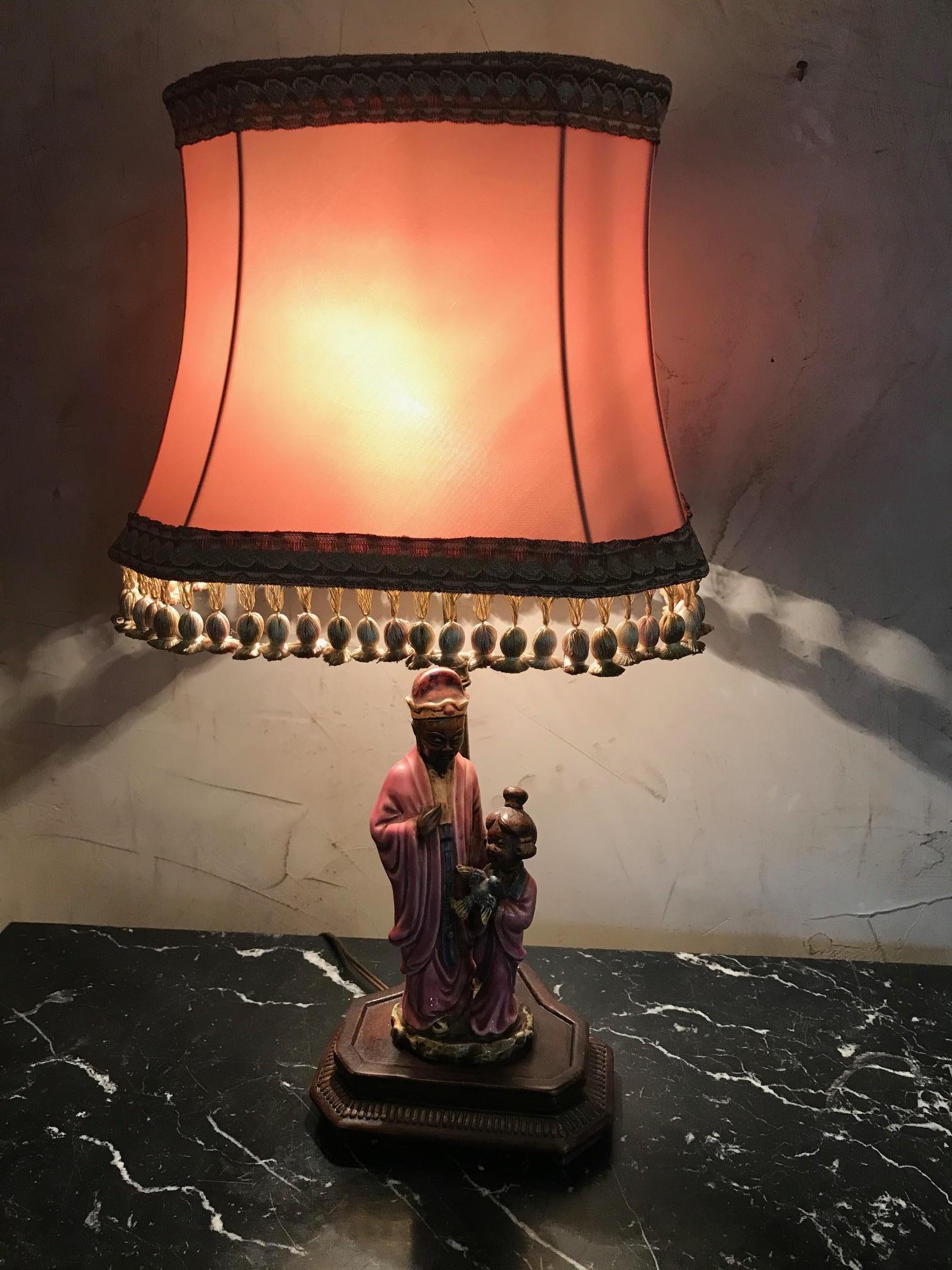 Beautiful 20th century Chinese style porcelain table lamp from the 1950s in good condition.
Representing a man and a girl holding a bird in her arms.
Nice pink lamp shade with fringes.
Wooden base. The height of the lampshade is adjustable.
  