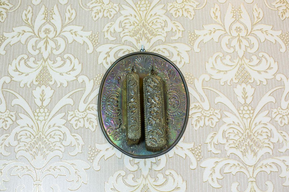 We present you a pair of old clothes brushes with natural bristles, with the wooden handles with a brass cap.
The brass parts are covered with an embossed pattern.
Together with the brushes, there is a tray with hooks for the brushes to be hung on