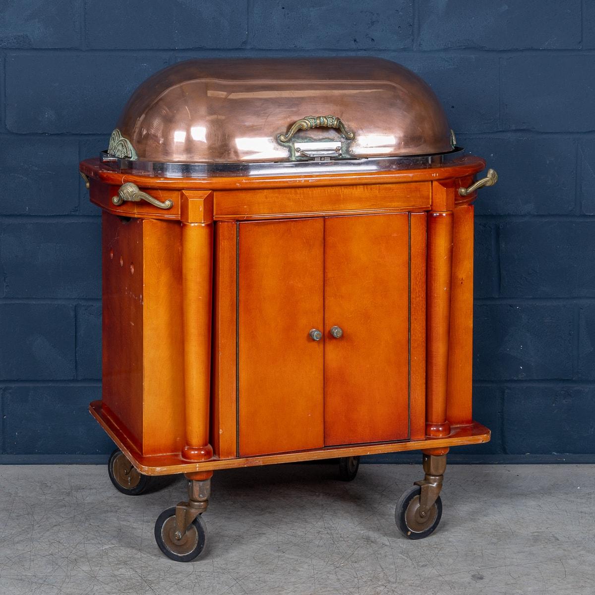 Un elegante carro de baño maría (o carnes hervidas), de finales del siglo XX, diseñado para elevar cualquier experiencia gastronómica. Con una llamativa tapa abovedada de cobre con bonitos detalles de latón, se complementa con un interior de acero