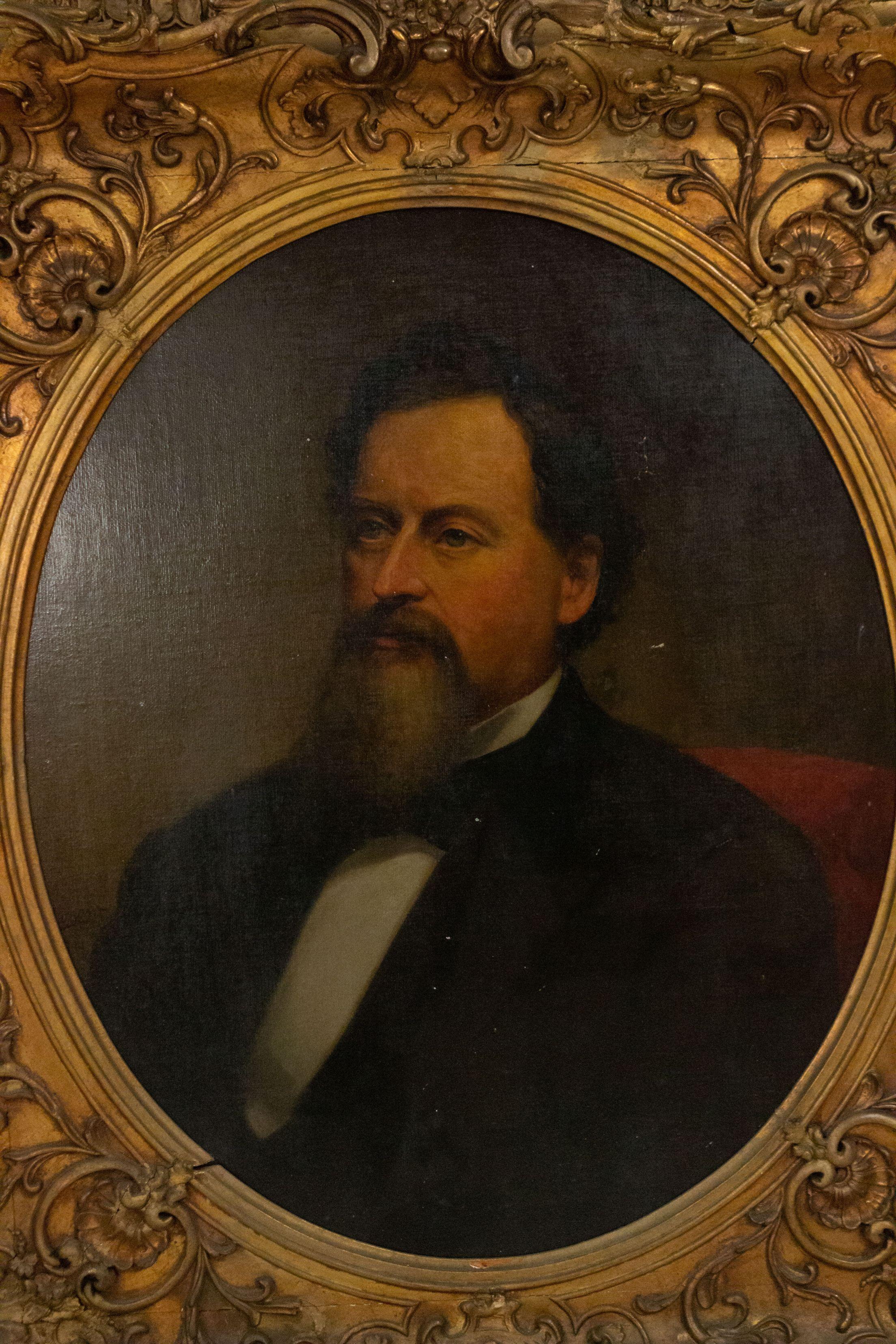 Gilt framed oval inset oil painting portrait of man with Van Dyke in red upholstered chair.
 