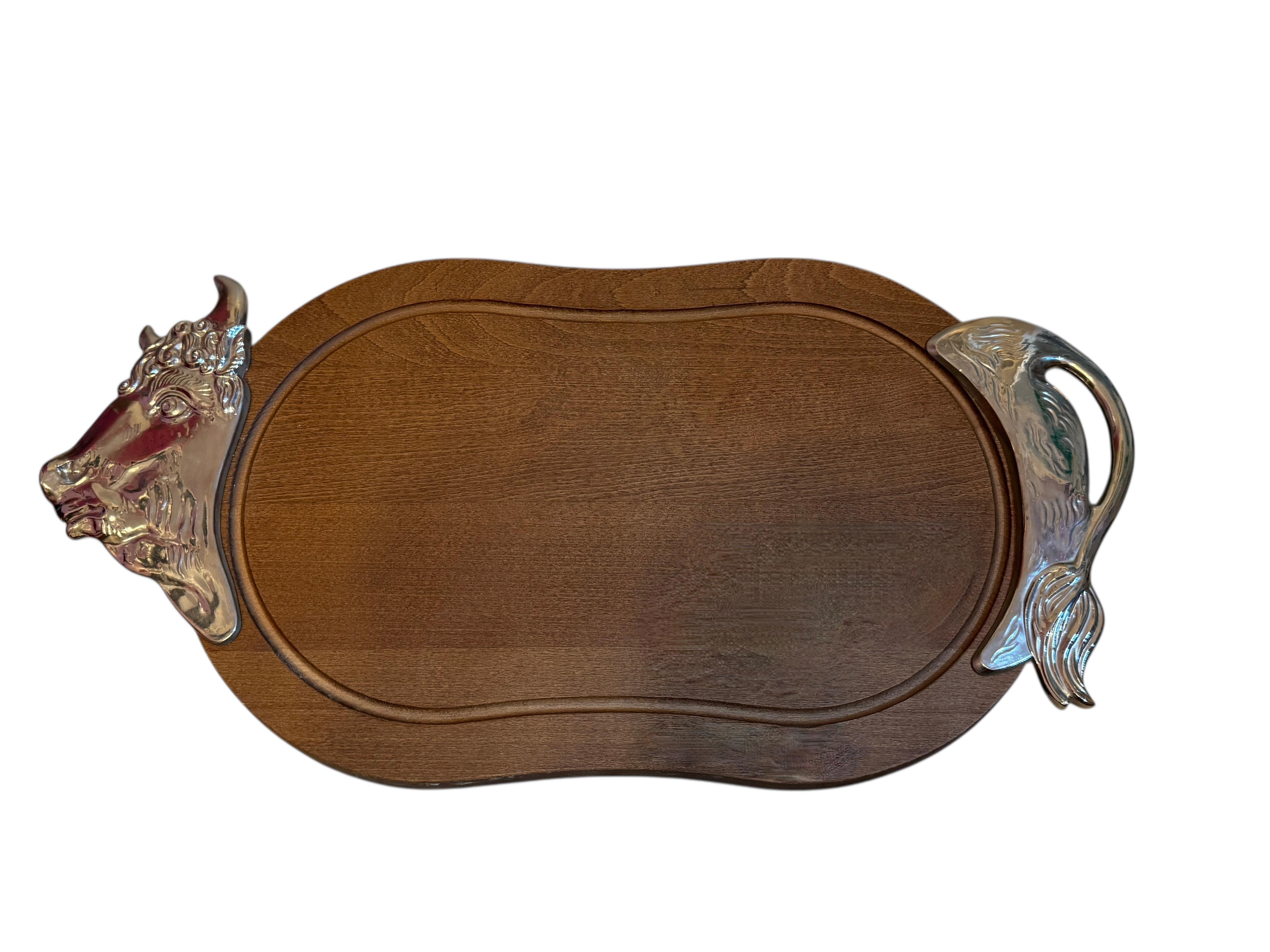 Cette planche à découper en forme de taureau est une pièce de service saisissante et sculpturale qui allie harmonieusement utilité et design fonctionnel. Fabriquée en bois richement teinté et accentuée par des détails en aluminium moulé, la pièce