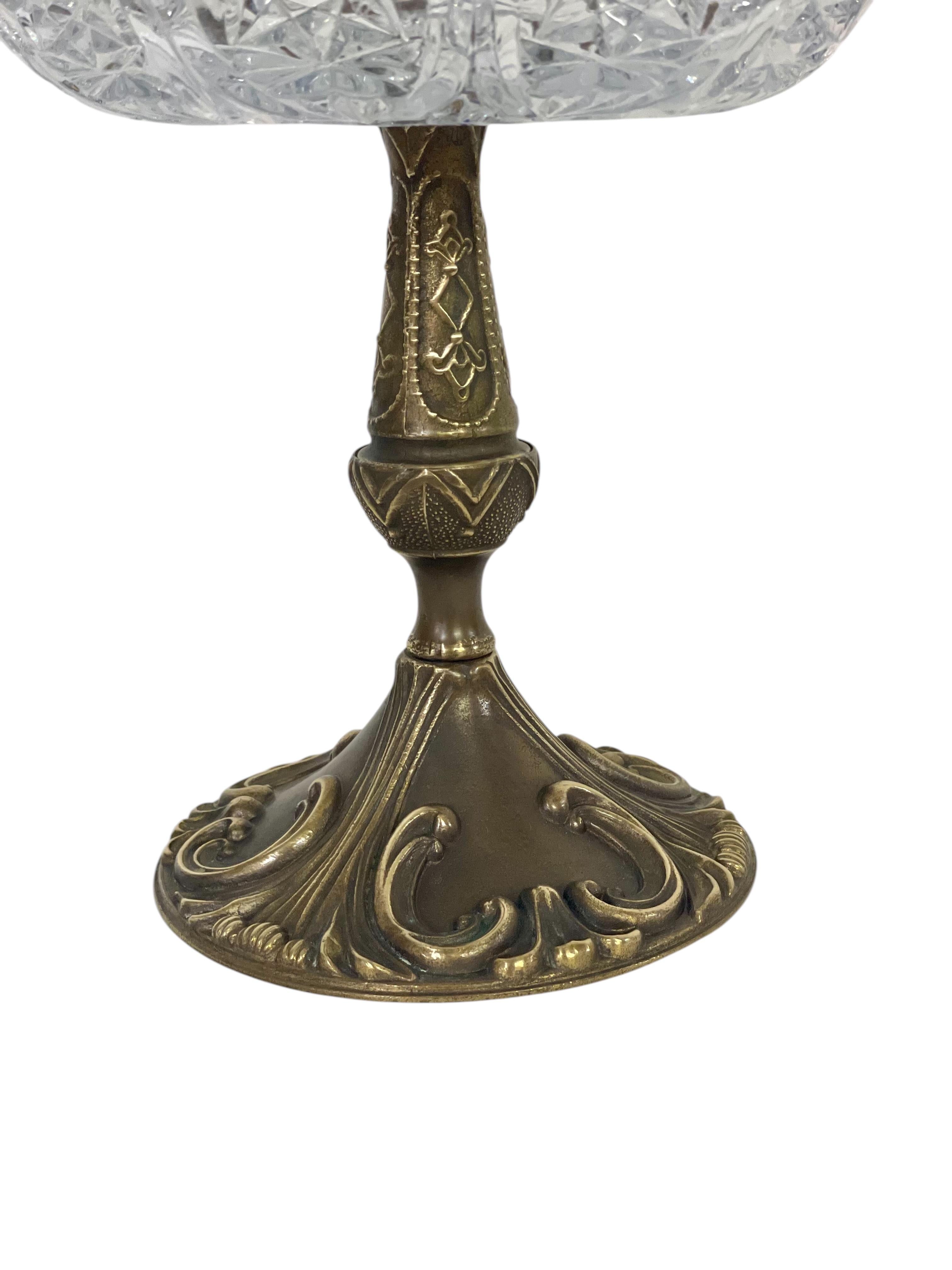 Este impresionante cuenco de cristal sobre un pedestal de latón dorado es una auténtica obra maestra de artesanía y diseño. El gran cuenco presenta intrincados cortes geométricos y facetas, que crean un deslumbrante juego de luces y sombras. El