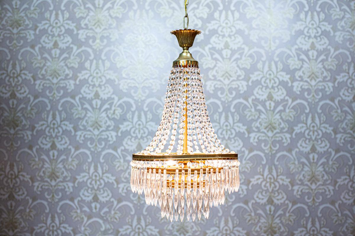 20th-Century Crystal Chandelier with Brass Elements

We present you this crystal chandelier combined with brass elements.
There are four sockets for E14 light bulbs.
The power source is 230 V.

Four crystals are missing. Other than that, the whole