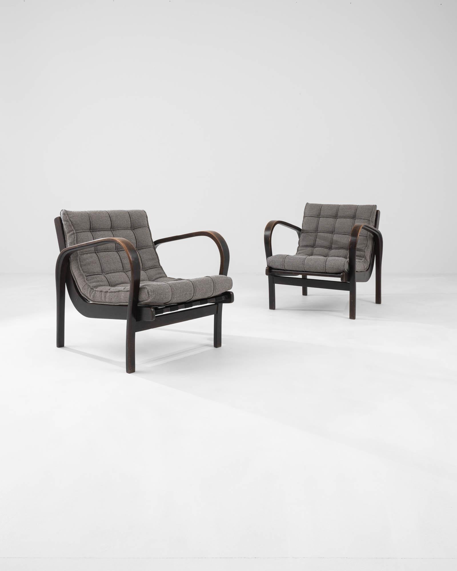 A pair of wooden upholstered armchairs created in 20th century Czechia by Kropȧček &
Koželka. Presenting a sleek yet inviting aura, this pair of chairs exudes a sense of classic mid-century character. Two sumptuously steam-bent arms float over the