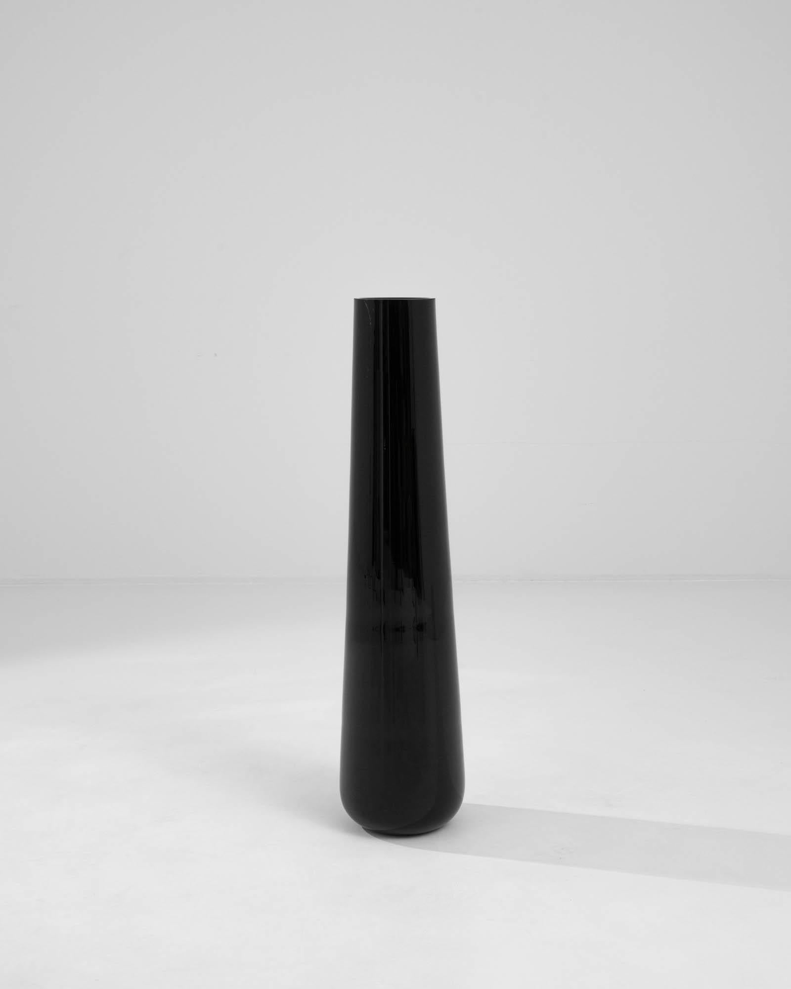 Embrace the understated sophistication of this 20th-century Czech glass vase. Dressed in a sleek black hue, the vase exudes an air of timeless elegance. Its elongated form gracefully ascends, adding a touch of refinement to any space. The simplicity