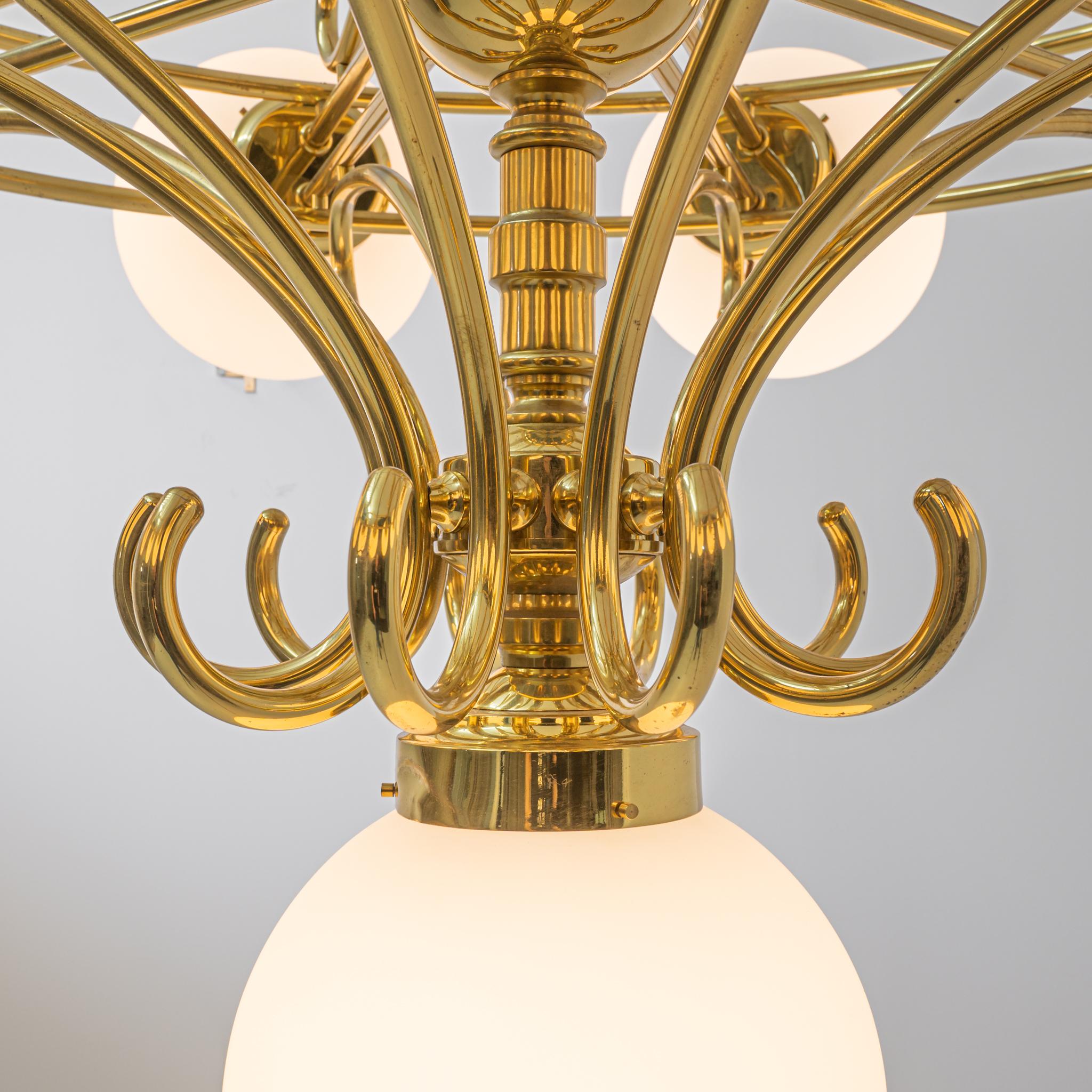 Bright and elegant, this vintage chandelier combines a baroque silhouette with the simplicity of Czech Mid Century design. Made in Czechia in the 20th century, frosted glass orbs form a crown of light around a wheel of brass, criss-crossed with