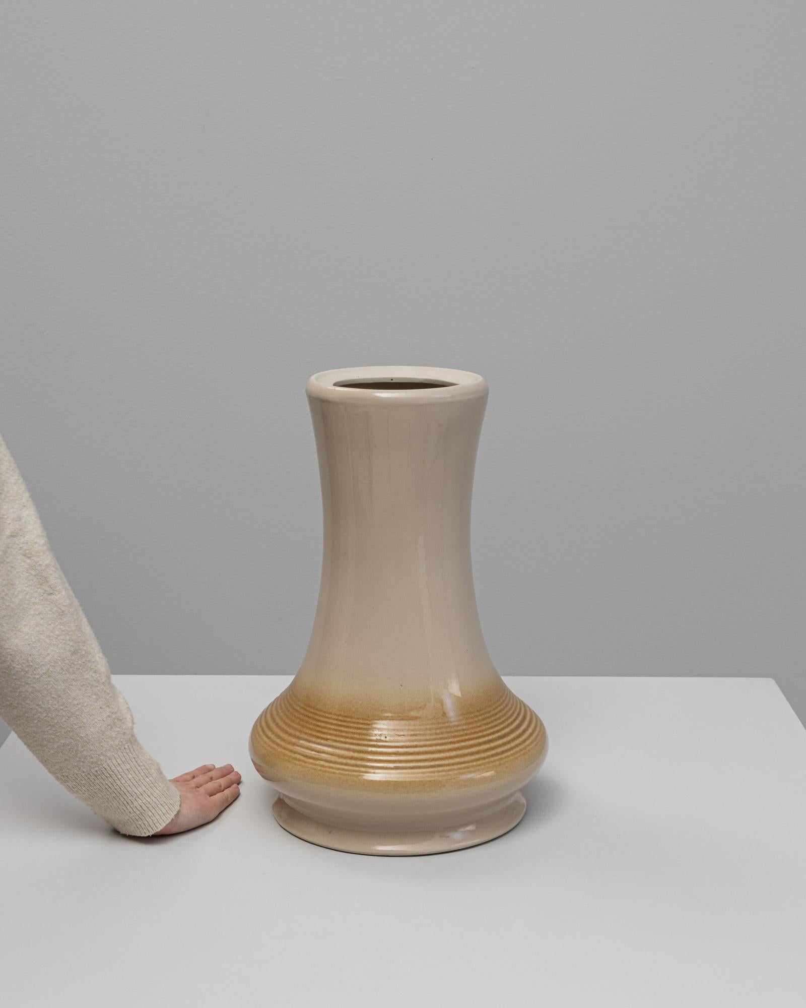 Cet élégant vase du milieu du siècle présente une silhouette aux contours doux, avec un col légèrement évasé et une base arrondie, caractéristiques du design moderniste tchèque. La glaçure lisse passe d'un beige chaud à un ton ambré doré près de la