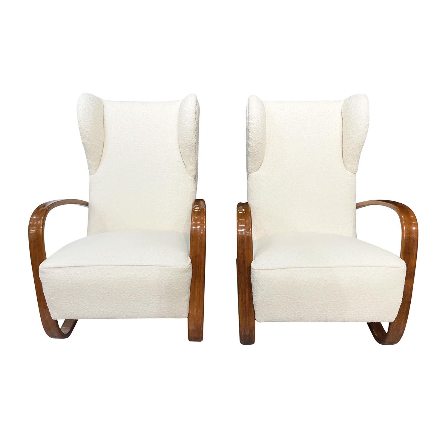 A light-brown, vintage Art Deco Czech pair of sculptural lounge chairs made of handcrafted polished Mahogany, designed by Jindrich Halabala in good condition. The seat backrest of the tall armchairs are inclined, detailed with earmuffs, headrests