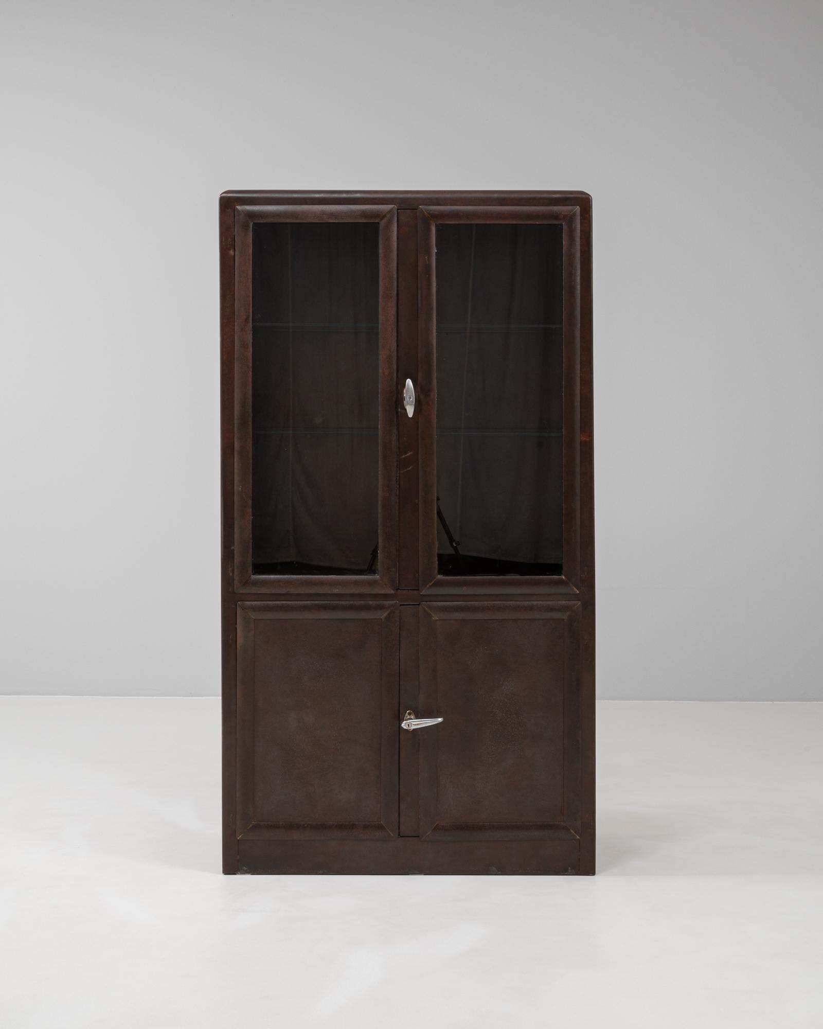This 20th Century Czech medical cabinet features a sleek, industrial design with a polished steel frame and deep, rich patina. Its two-part construction includes an upper section with glass-paneled doors and adjustable shelving, ideal for displaying