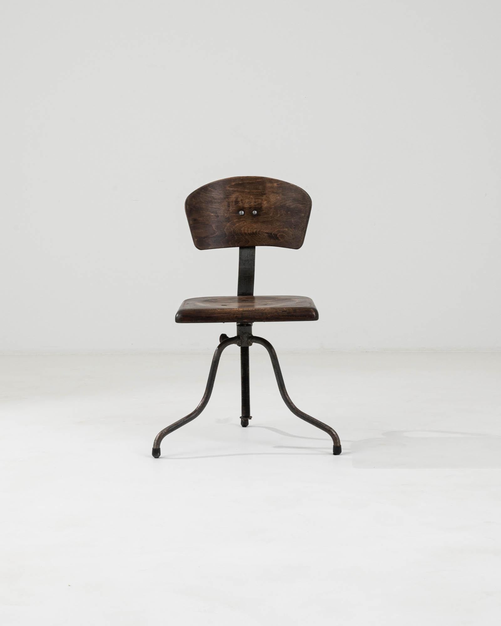 Capture the essence of industrial chic with this 20th Century Czechia Industrial Lifting & Swivel Chair, a piece that perfectly marries form and function. The chair boasts a solid wood seat and backrest, each piece rich in dark, swirling wood grains