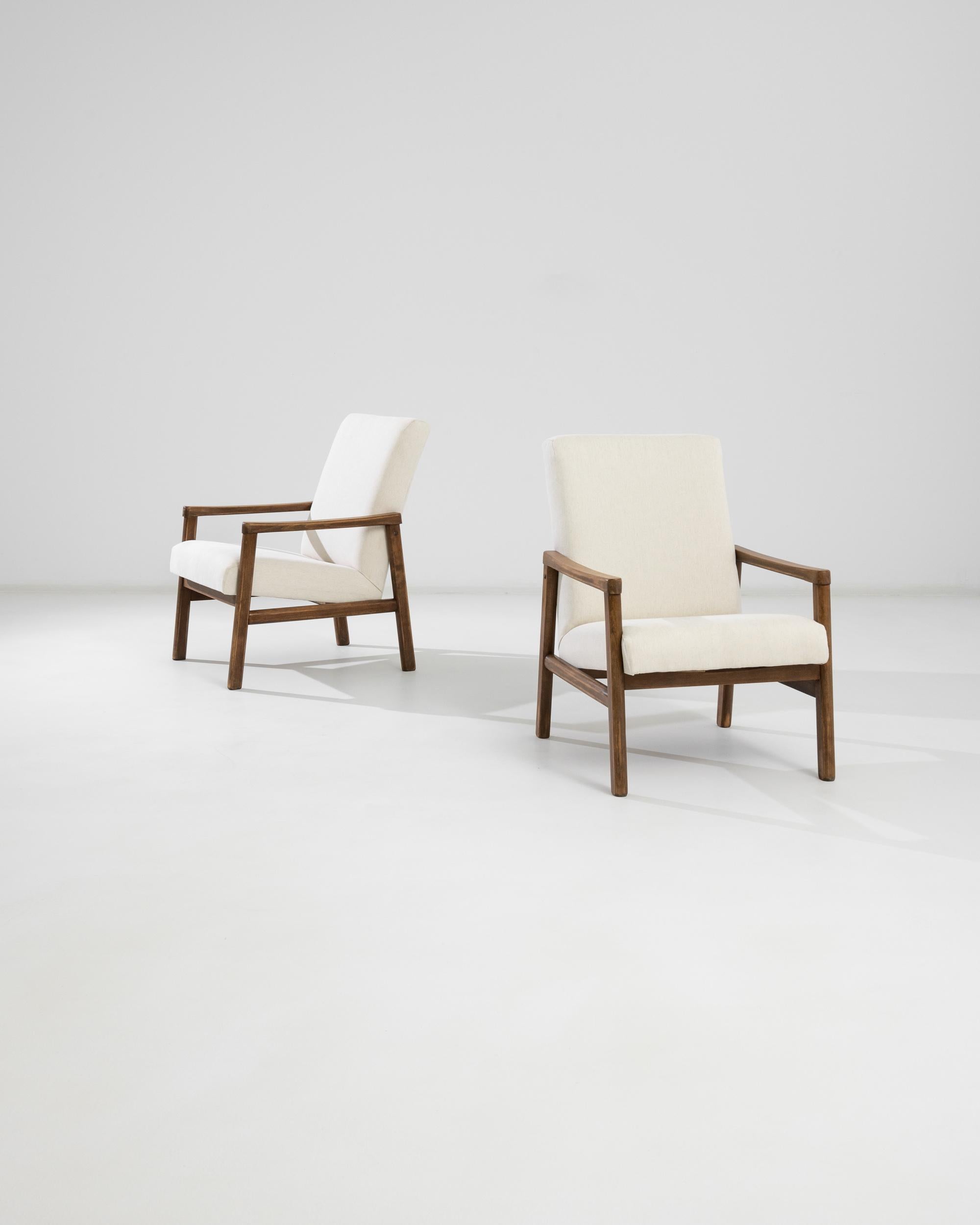 This pair of 20th-century wooden armchairs from Czechia embodies mid-century minimalist charm combined with functionality. Featuring a warm, natural wood frame, these armchairs are designed with sleek lines and gently curved armrests that offer a