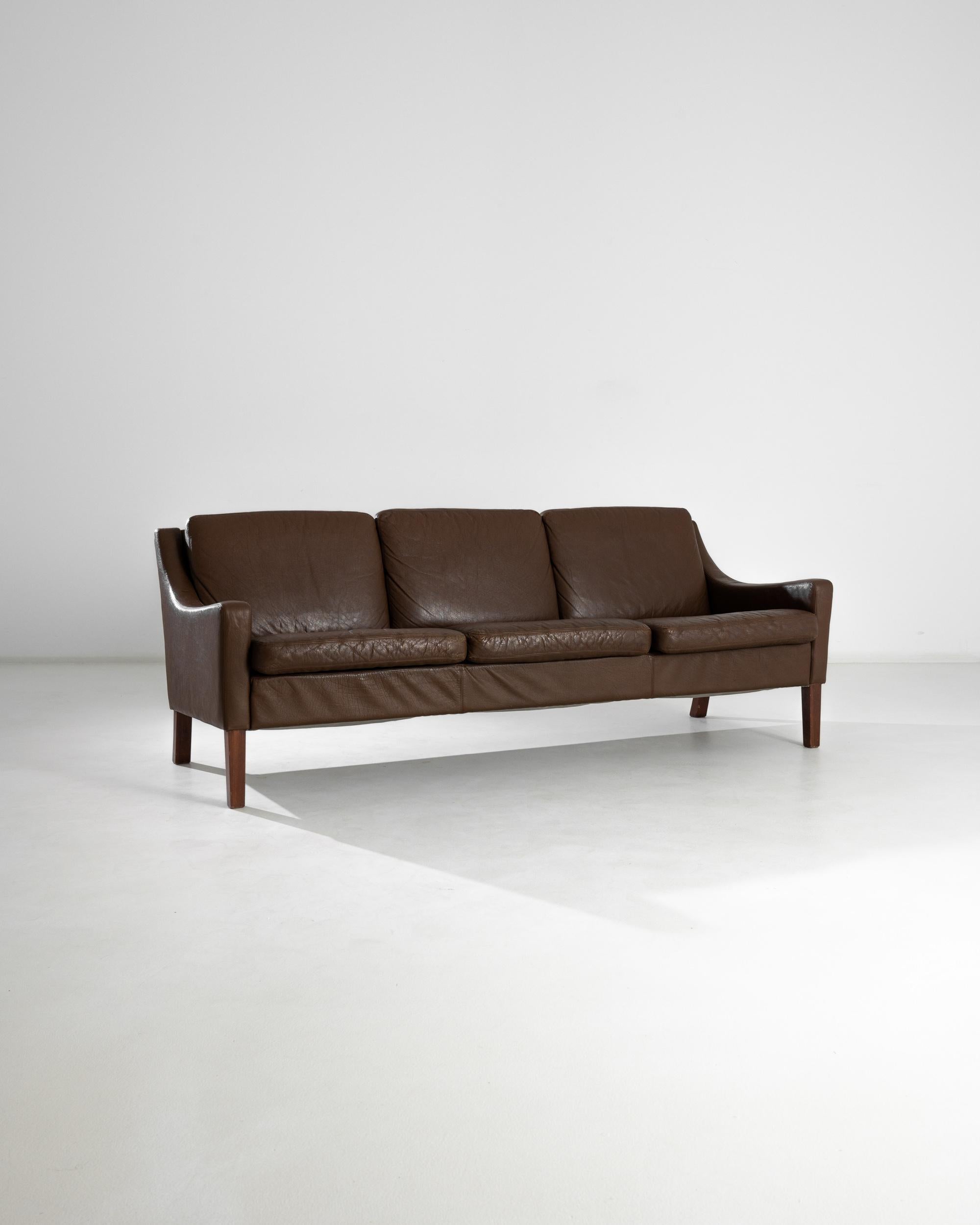 Ein Ledersofa aus Dänemark, hergestellt im 20. Jahrhundert. Ein wunderschönes Dreisitzer-Sofa im Vintage-Stil, umhüllt von prächtigem braunem Leder. Auf vier quadratischen Beinen stehend, befindet sich dieses Stück am Schnittpunkt verschiedener