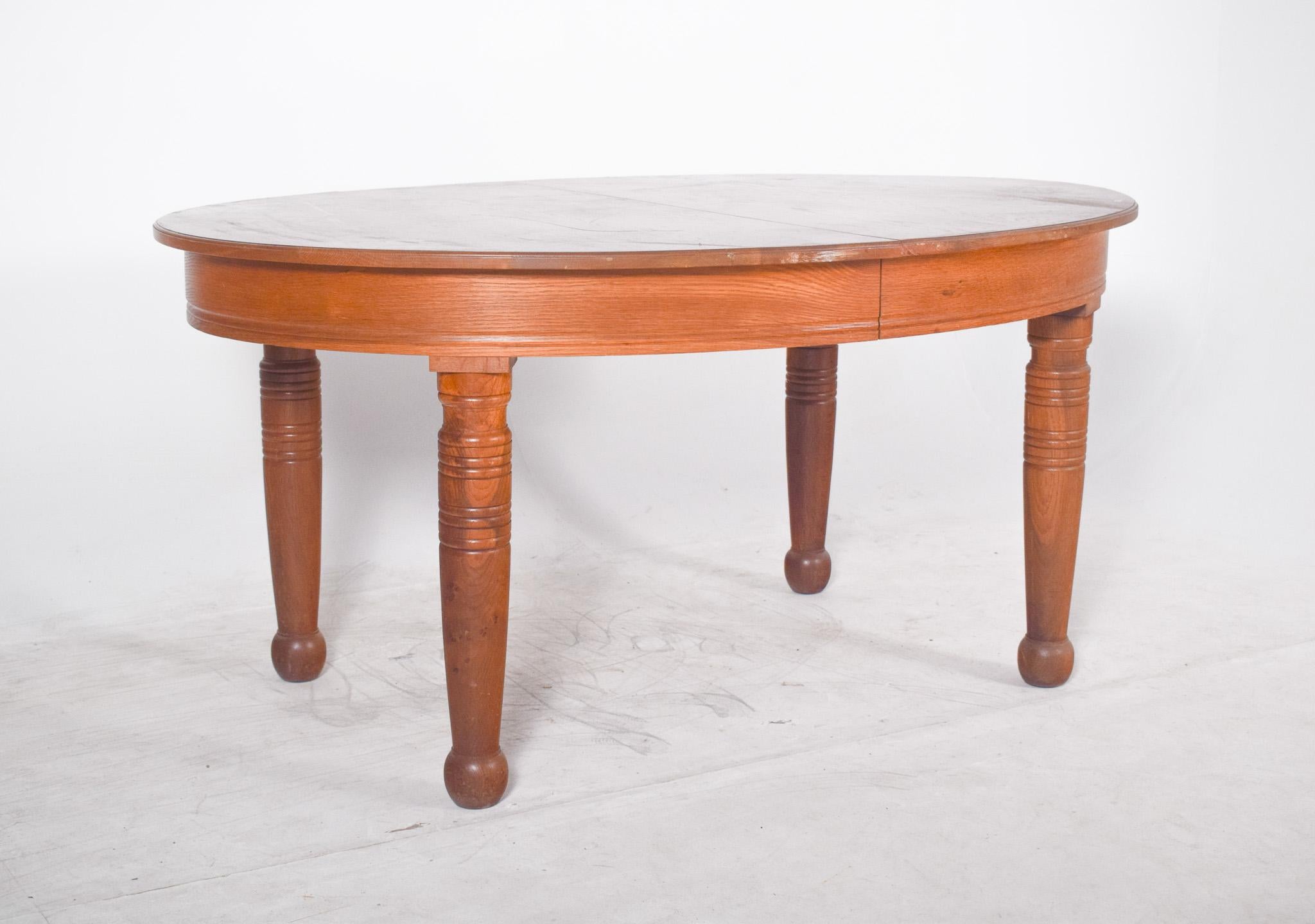 Oval oak dining table. It has a classic shape with gently rounded edges, offering a cosy, traditional touch to the space in which it sits. It stands on four sturdy cylindrical legs, turned with decorative rings and ending in rounded feet that