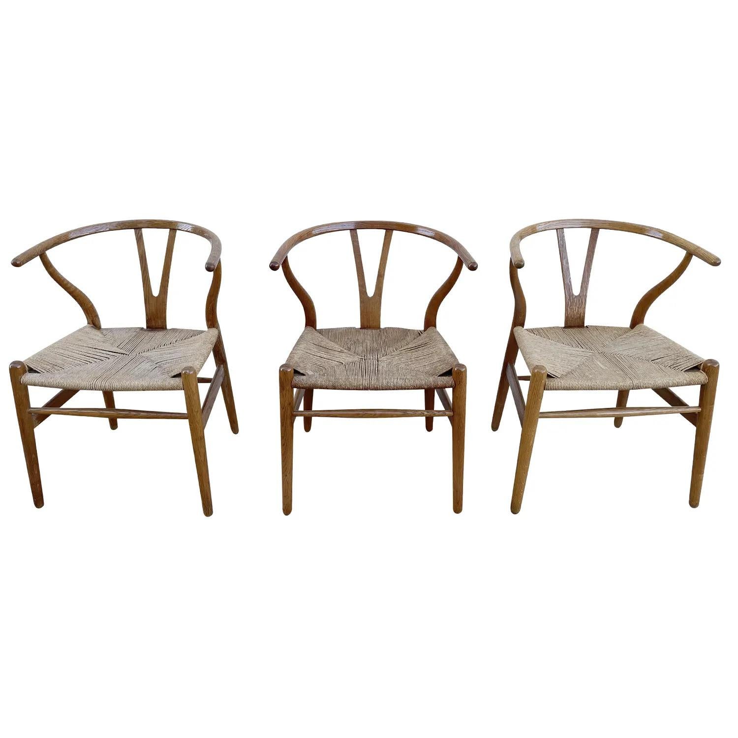 A light-brown, vintage Mid-Century Modern Danish set of three Wishbone chairs made of hand carved Oakwood, designed by Hans J. Wegner and produced by Carl Hansen & Søn, in good condition. The Scandinavian Y-shaped, armchairs have a curved slim