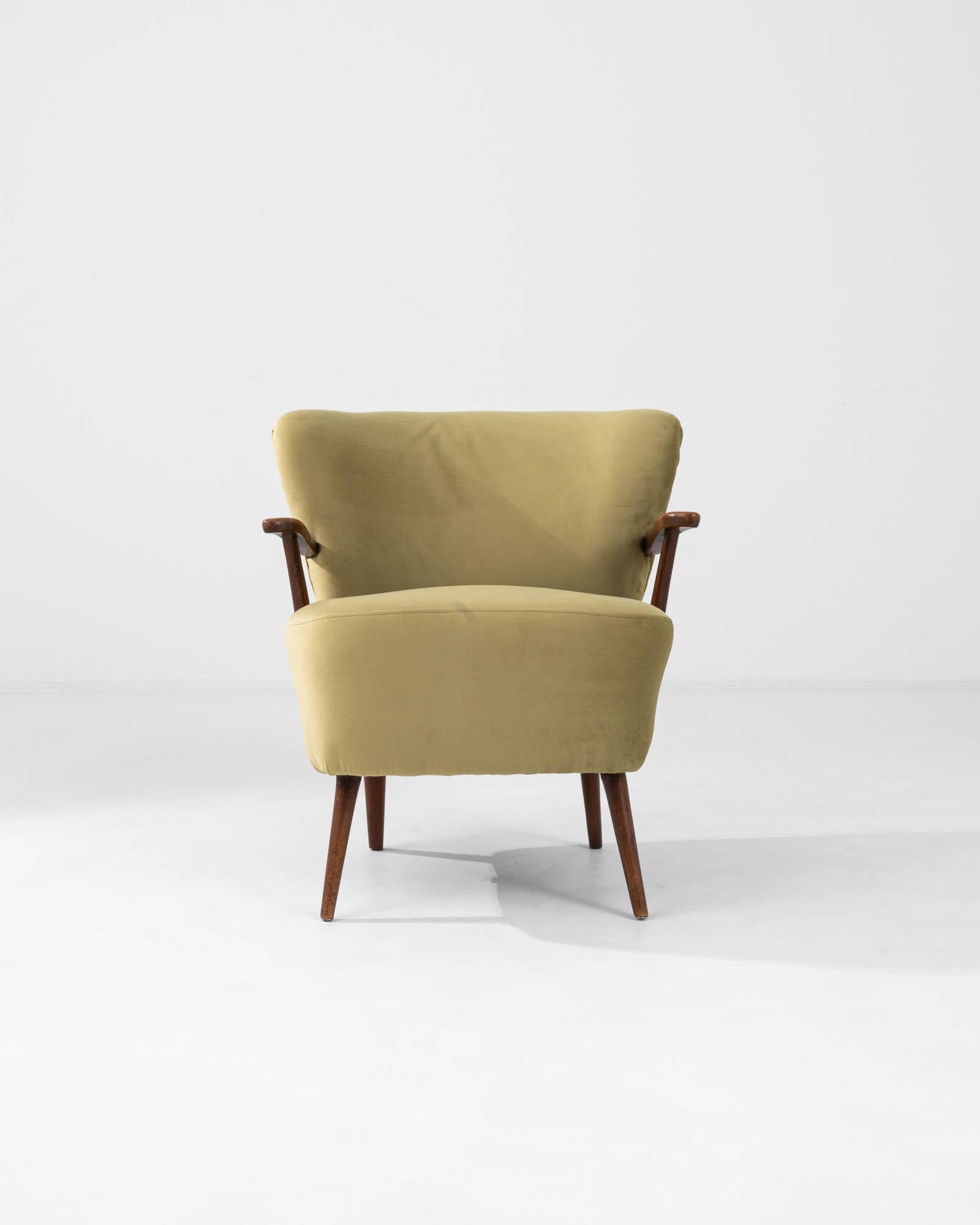 Experience the warmth and allure of this 20th Century Danish Upholstered Armchair, a singular piece that captivates with its understated beauty. Wrapped in a textured olive-yellow fabric, it offers a cheerful and inviting ambiance. The chair’s sleek