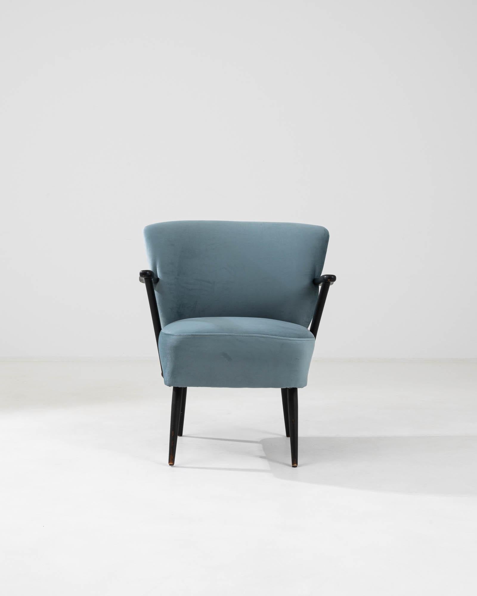 This 20th Century Danish upholstered armchair is a celebration of minimalist design and comfort. Enveloped in a plush, velvety teal fabric, it invites you to embrace its softness with every touch. The chair's sleek black armrests add a modern twist,