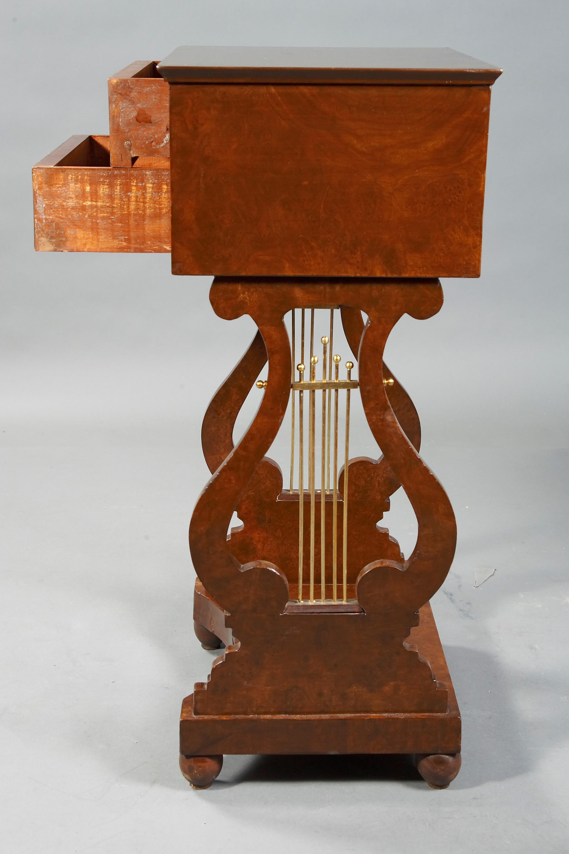 Nogal oscuro sobre madera blanda maciza. Base recta de marco de dos cuerpos sobre carrilleras caladas en forma de lira con laterales metálicos. Placa base retráctil por cuatro lados. Cajón superior con compartimentos. Placa rectangular saliente.