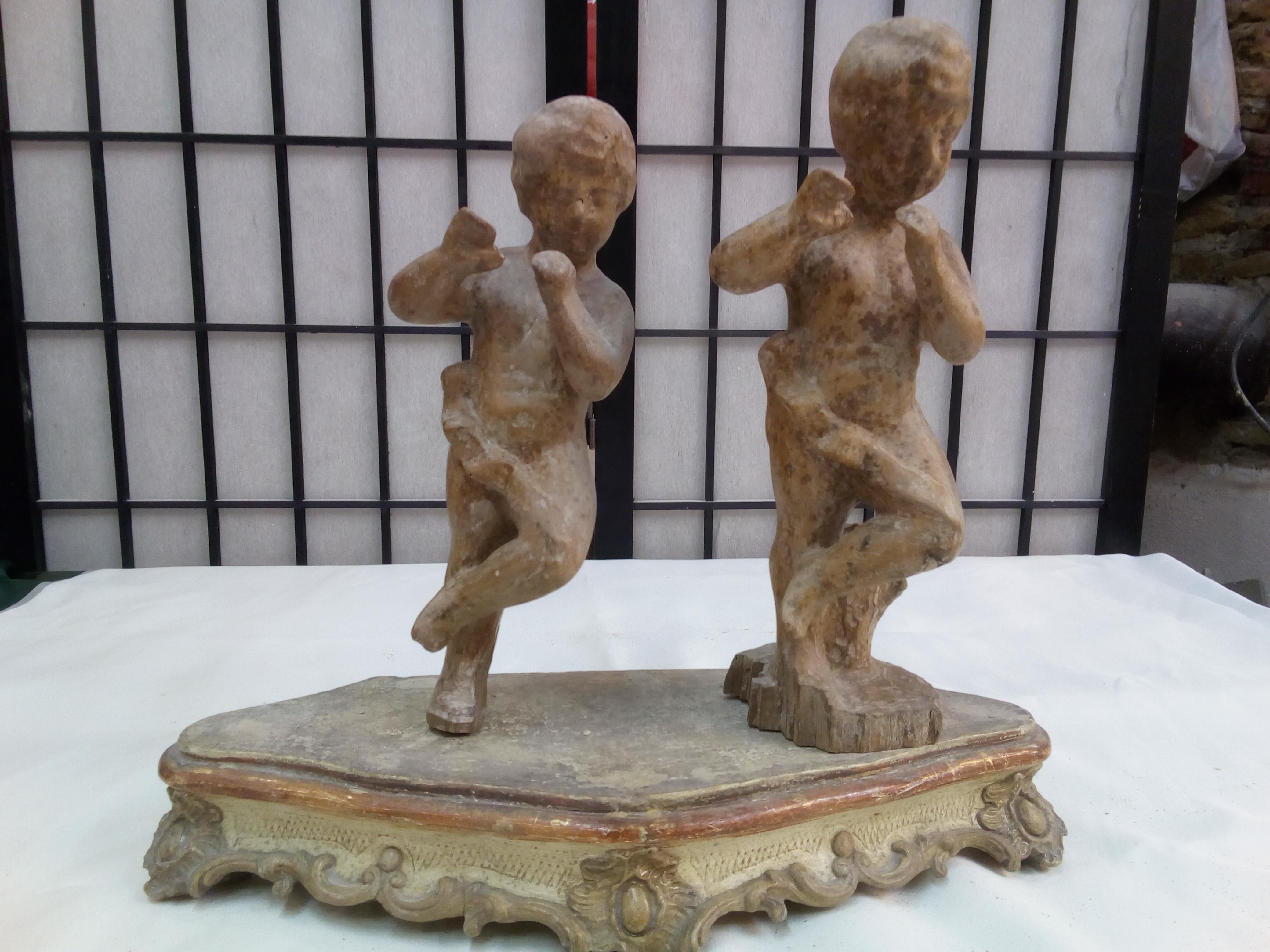 A couple of hand-carved Musicians in wood inserted into a non-coeval base.
The subjects represent two dancing children playing the flute. 
This sculpture piece is of perfect size to be a desk accessory, measuring 11x31x26 cm (4x12x10 inches).

This