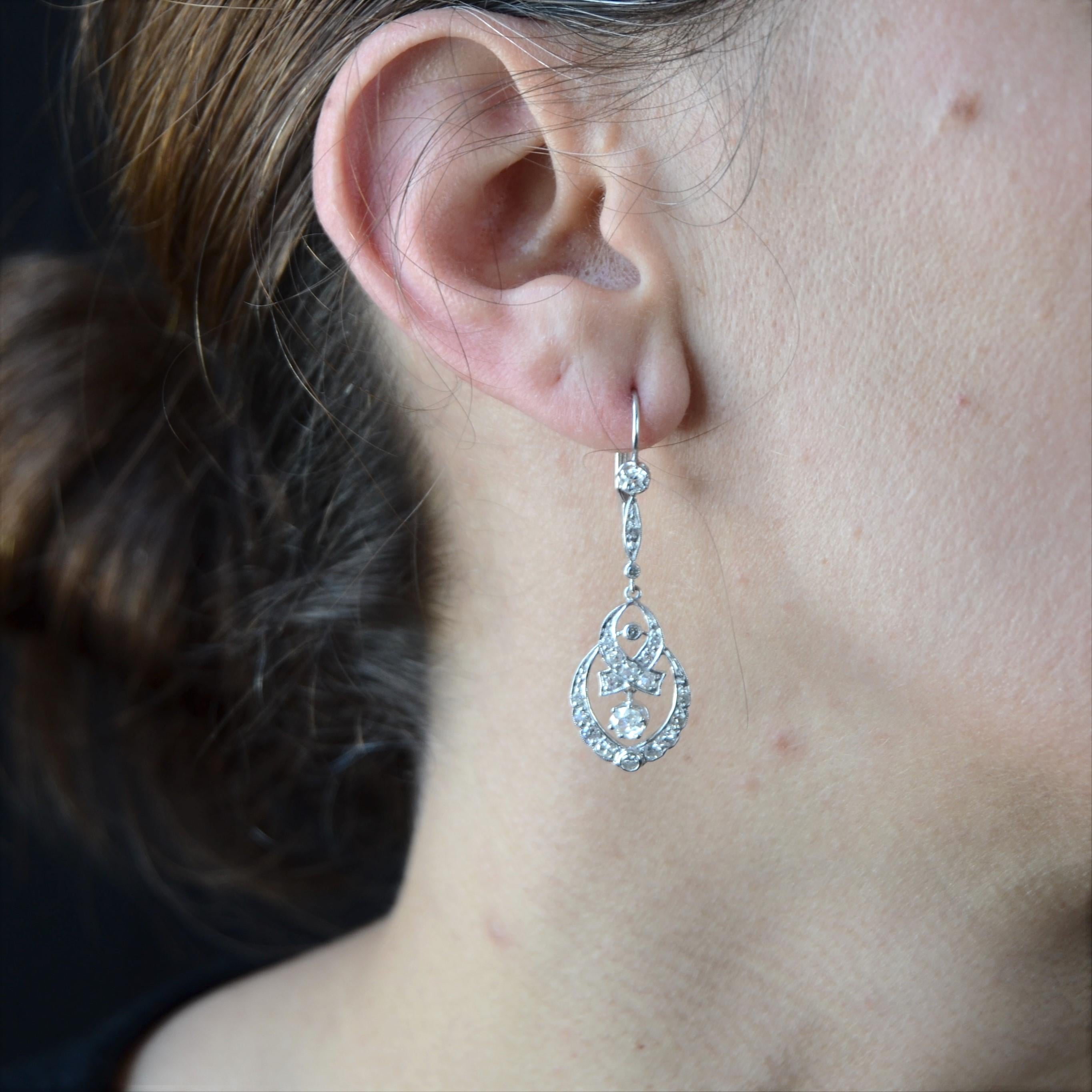 For pierced ears.
Earring in 18 karat white gold.
Feminine antique ear pendant, each one is constituted of a pattern formed of an antique cushion- cut diamond retained with claws, and of a shuttle set with a brilliant- cut diamond, another small