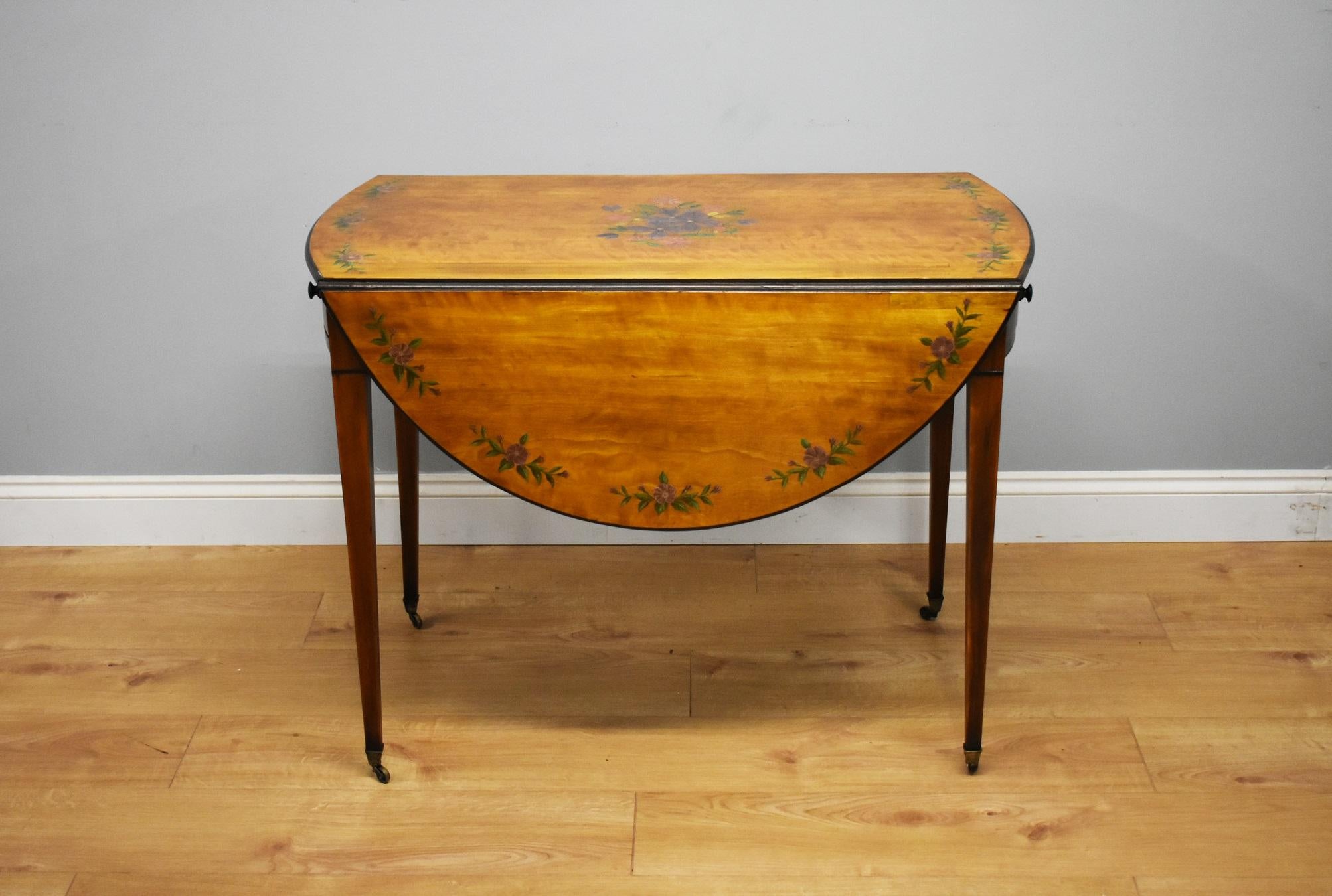 For sale is a fine Edwardian hand painted satinwood pembroke table. The top of the table is decorated with floral swags, with further floral work to the centre. There is a lift up flap on either side, which when open further compliments the top with