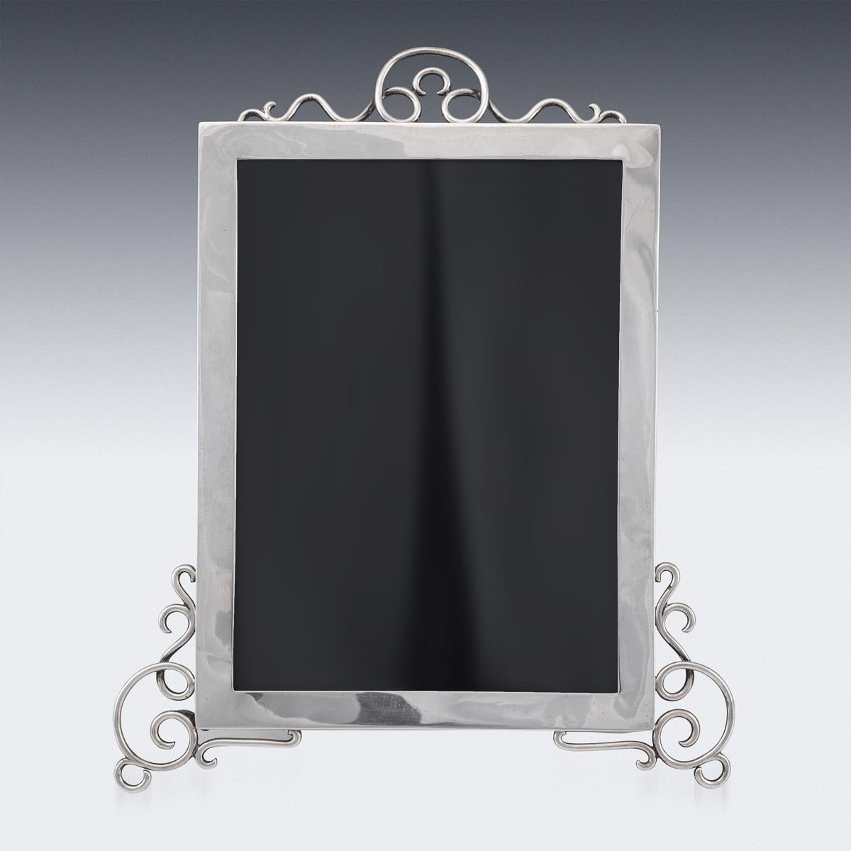 Antique early-20th century Edwardian solid silver photograph frame, of particularly large size, applied with scrolls and standing on scroll feet, mounted on a back with easel support, front with beveled glass to protect the photo. Hallmarked English