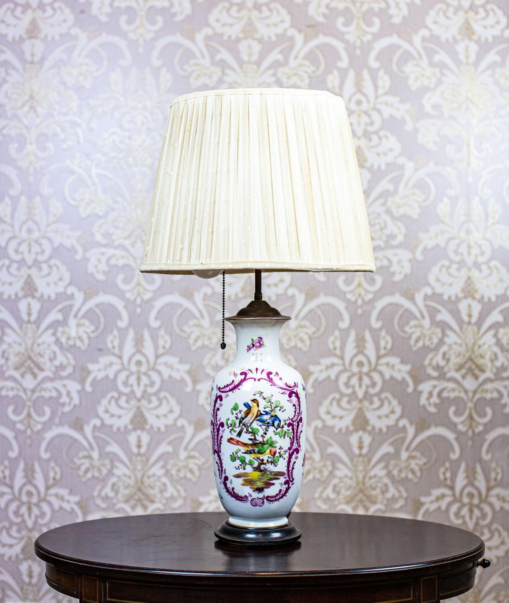 20th-Century Electric Table Lamp with Decorative Ceramic Base

We present you an electric table lamp from the mid. 20th century.
The ceramic base is decorated with patterns depicting nature. The shade is made of a fabric.
The source consists of two
