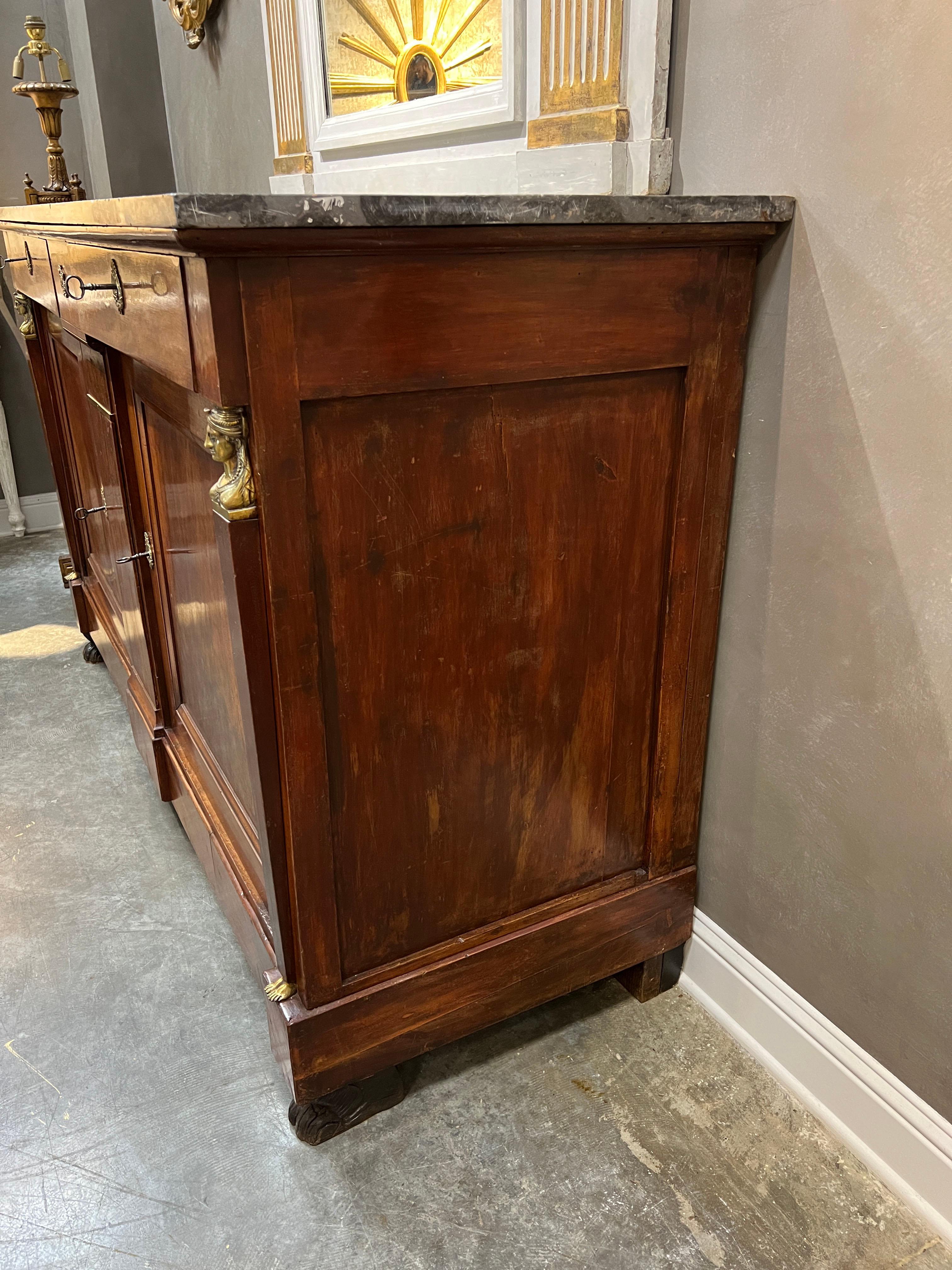 Impressive grande Empire style two door buffet in mahogany with original marble top. The cabinet is accented with brass key escutcheons and with a caryatided bust and feet at top and bottom of side columns. Top drawers in pine lined with green felt.