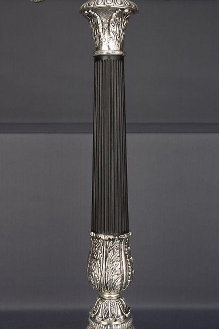 Monumentaler Kandelaber im Empire-Stil.
Bronze, fein graviert und versilbert. Chanel-Säulen mit schwarzer Patinierung, als Halterung für vier geschwungene Kandelaberarme.

(T-Ra-14).