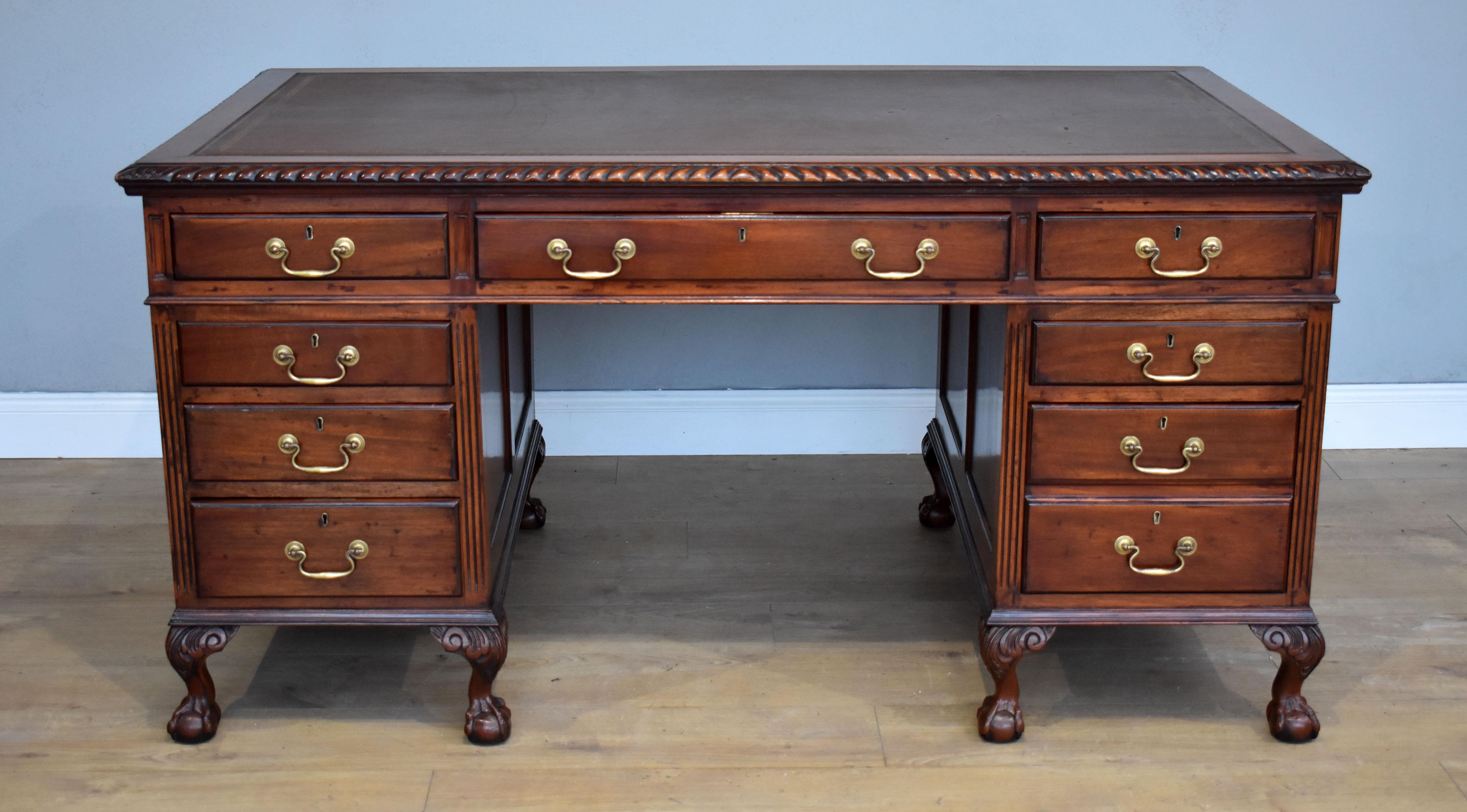 For sale is an early 20th century Chippendale style mahogany pedestal desk. The top inset with its original writing surface, above a gadrooned edge, with three drawers below. The top fits onto two pedestals, each with three graduated drawers. The